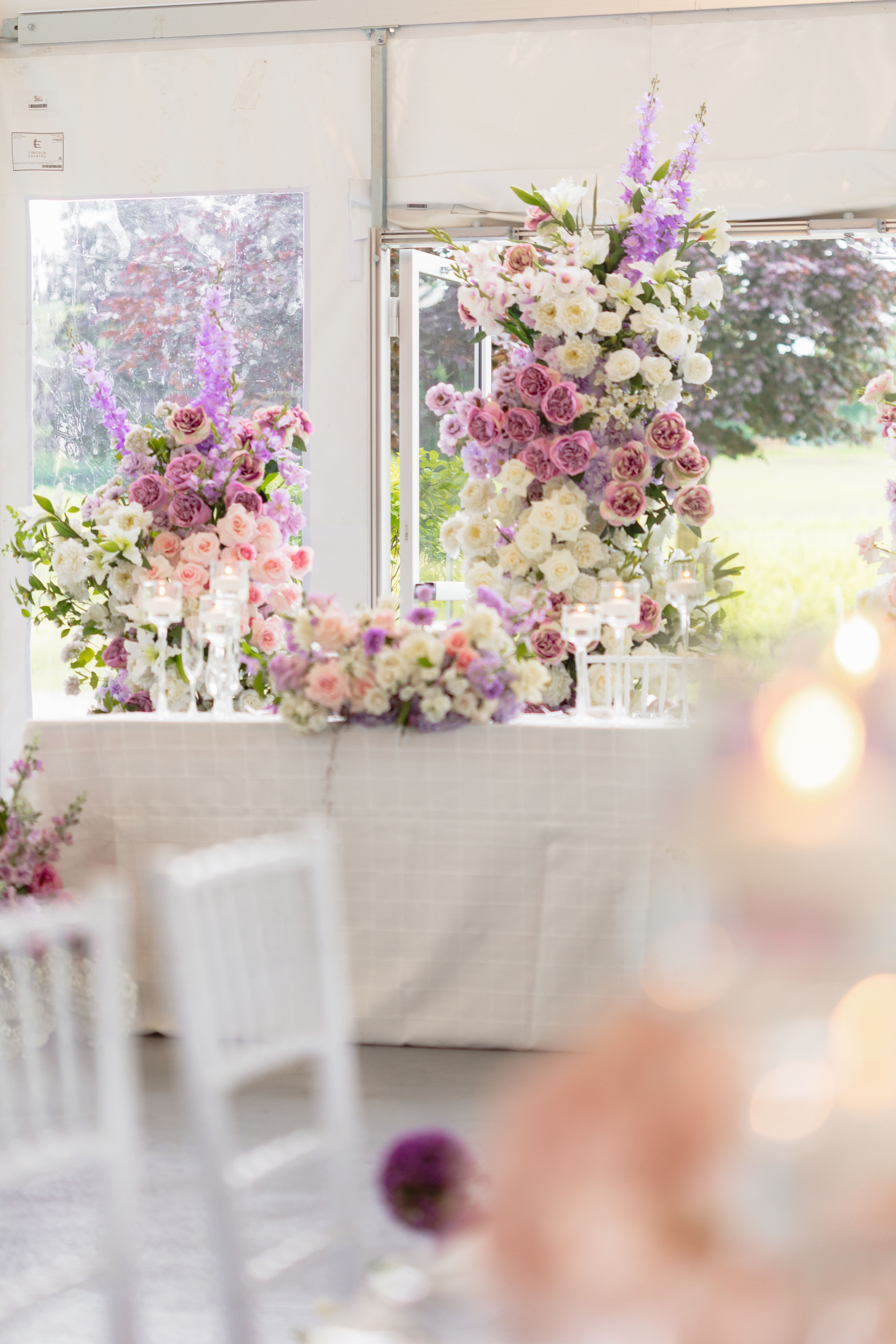 Pink, purple and white floral arrangements behind a white reception table inside the tent at Lincoln Estates.