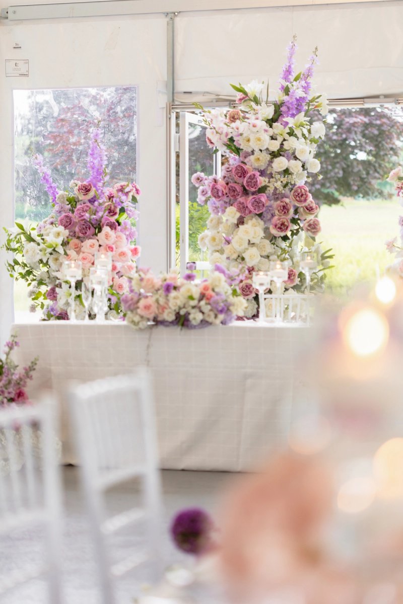 Pink, purple and white floral arrangements behind a white reception table inside the tent at Lincoln Estates.