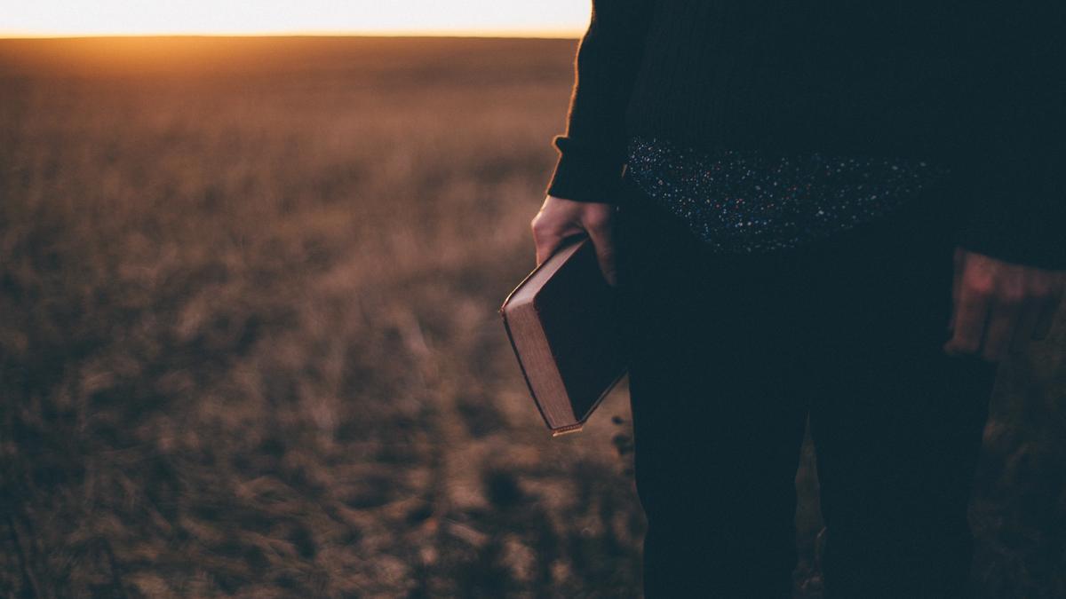 Mann som står på et jorde med en bok i hånden. Illustrasjonsbilde tatt av Priscilla Du Preez fra Unsplash