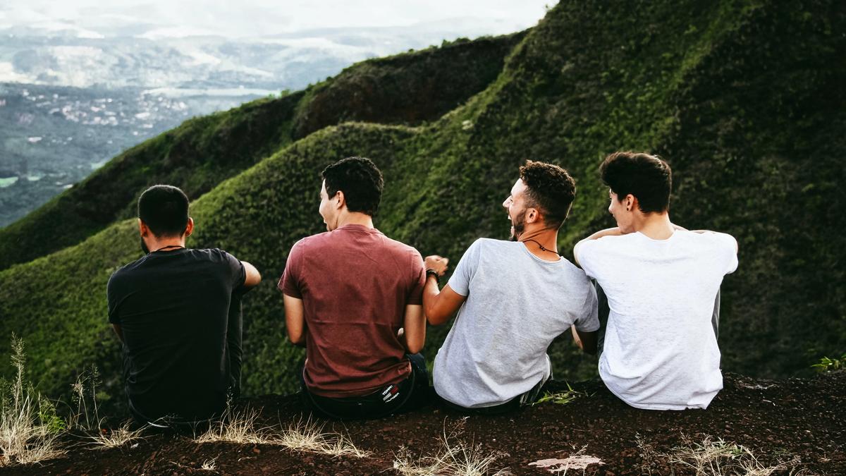 Fire menn som sitter på en fjellkant, med utsikt over grønne fjell.