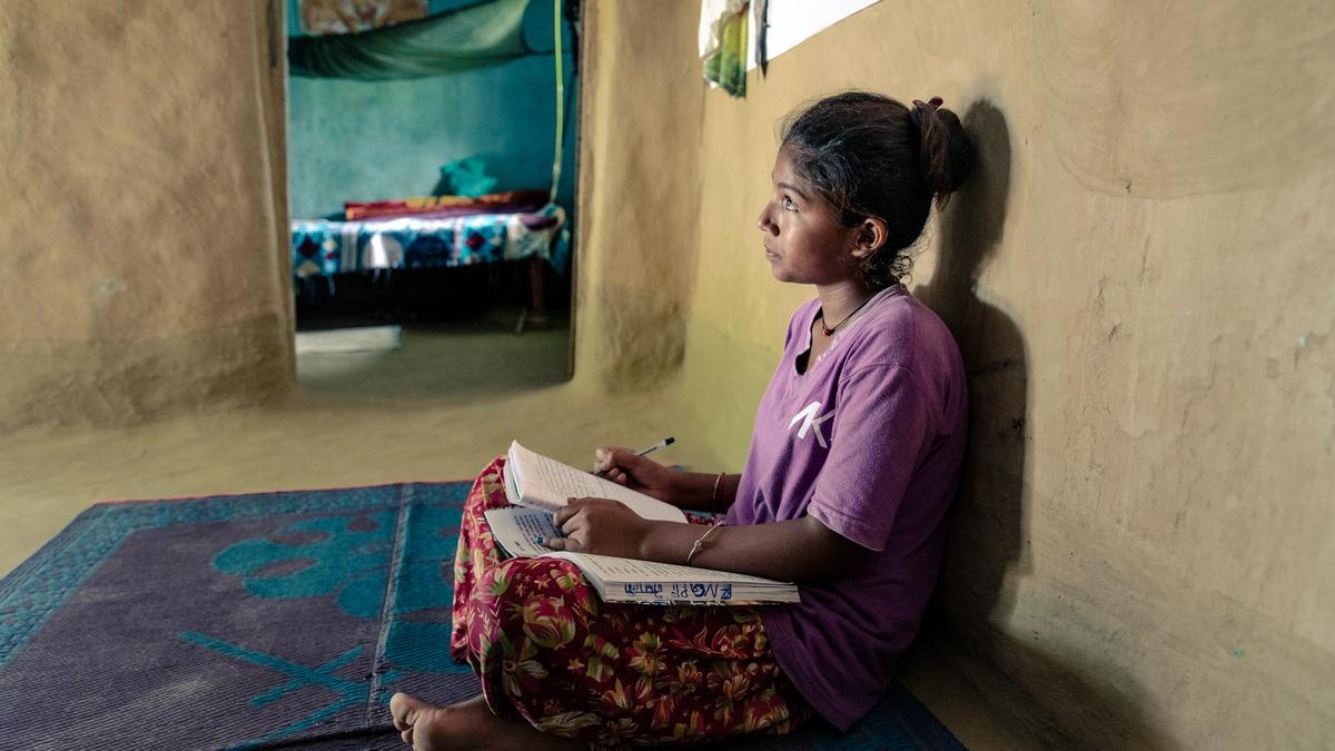 Bilde av en ung jente som sitter på gulvet med bena i kryss med ryggen lent mot veggen. I fanget har hun en notatbok og skolebok og hun holder en penn i ene hånden. Blikket hennes er hevet mot noe annet som ikke vises i bildet.Bilde tatt i Nepal av Eirik Thallaug, Plan Norge. 
