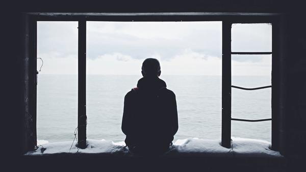 Illustrasjonsbilde av en mann som sitter i et vindu og ser utover havet tatt av Noah Silliman fra Unsplash