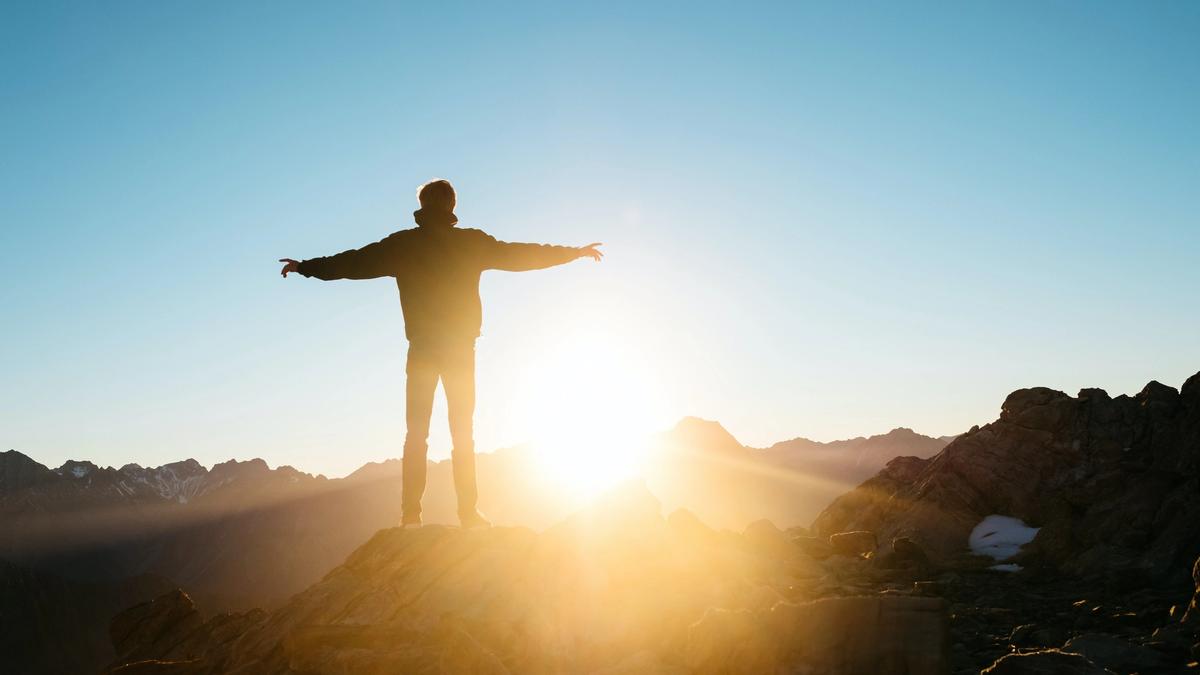 Illustrasjonsbilde av en mann som har armene ut mens han står å ser utover et fjell-landskap og en solnedgang. Bildet er tatt av Pablo Heimplatz fra Unsplash