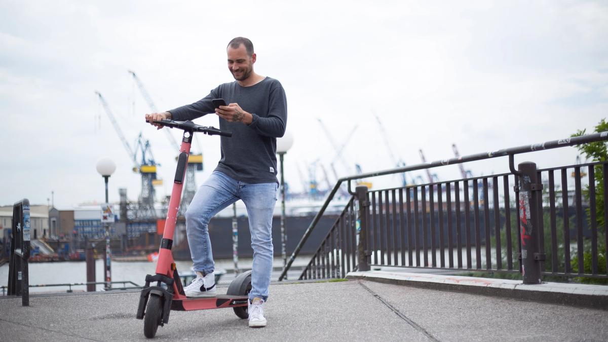 Illustrasjonsbilde av en mann som står og holder en e-sparkesykkel og bruker mobiltelefonen sin, tatt av Christina Spinnen fra Unsplash