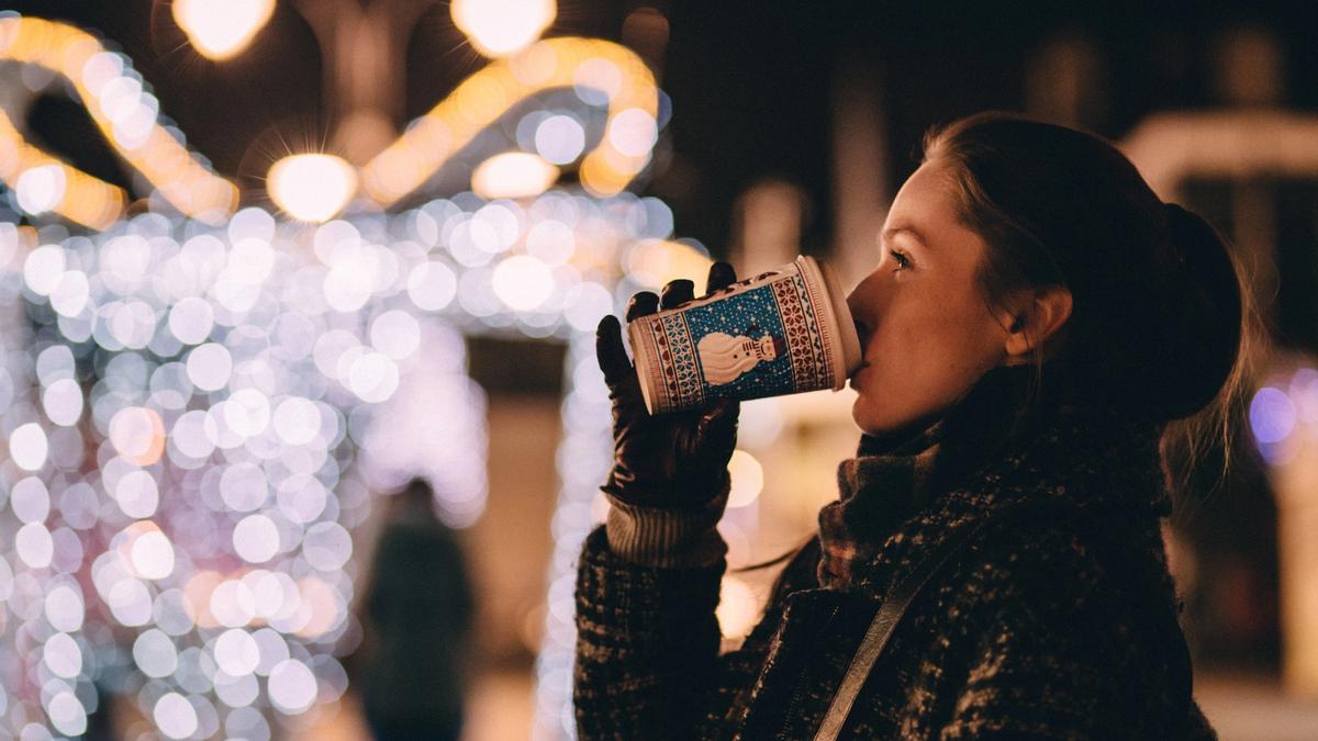 Kvinne drikker fra ett julepappbeger ute omringet av julelyst
