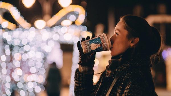 Kvinne drikker fra ett julepappbeger ute omringet av julelyst 