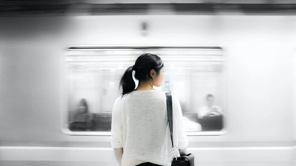 Illustrasjonsbilde av kvinne med mørkt hår som står og ser på en t-bane som går fort forbi, tatt av Eutah Mizushima fra Unsplash