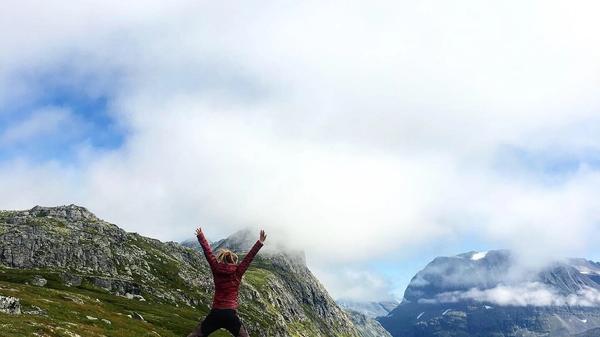 Kvinne som hopper på fjellet. Blå himmel med skyer bak grønne fjell. Bilde privat, Tine Norderhaug 