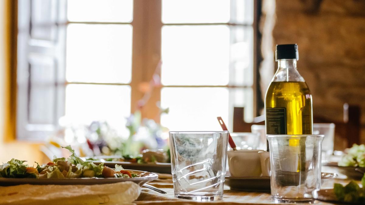 Olivenolje på ett spisebord med mat og glass rundt seg