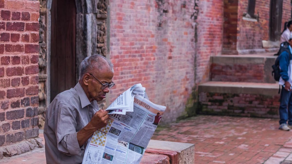 Illustrasjonsbilde av en eldre mann som sitter å leser avisen på en mursteinkant tatt av Aalok Atreya fra Unsplash