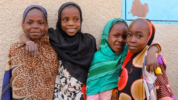 Bilde av fire jenter i Niger som har på seg fargerike klær, holder rundt skuldrene til hverandre og smiler. Bilde tatt i Niger av Amina Issa Oumarou, Plan International.