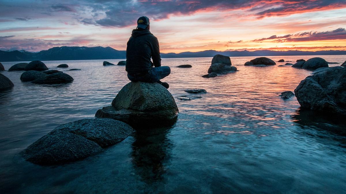 Illustrasjonsbilde av mann som sitter på en stein ved sjøen. Tatt av Keegan Houser fra Unsplash