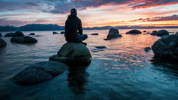 Illustrasjonsbilde av mann som sitter på en stein ved sjøen. Tatt av Keegan Houser fra Unsplash