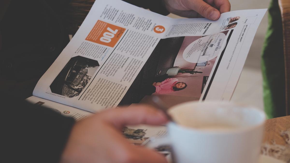 En person leser avisen med en stor kaffekopp