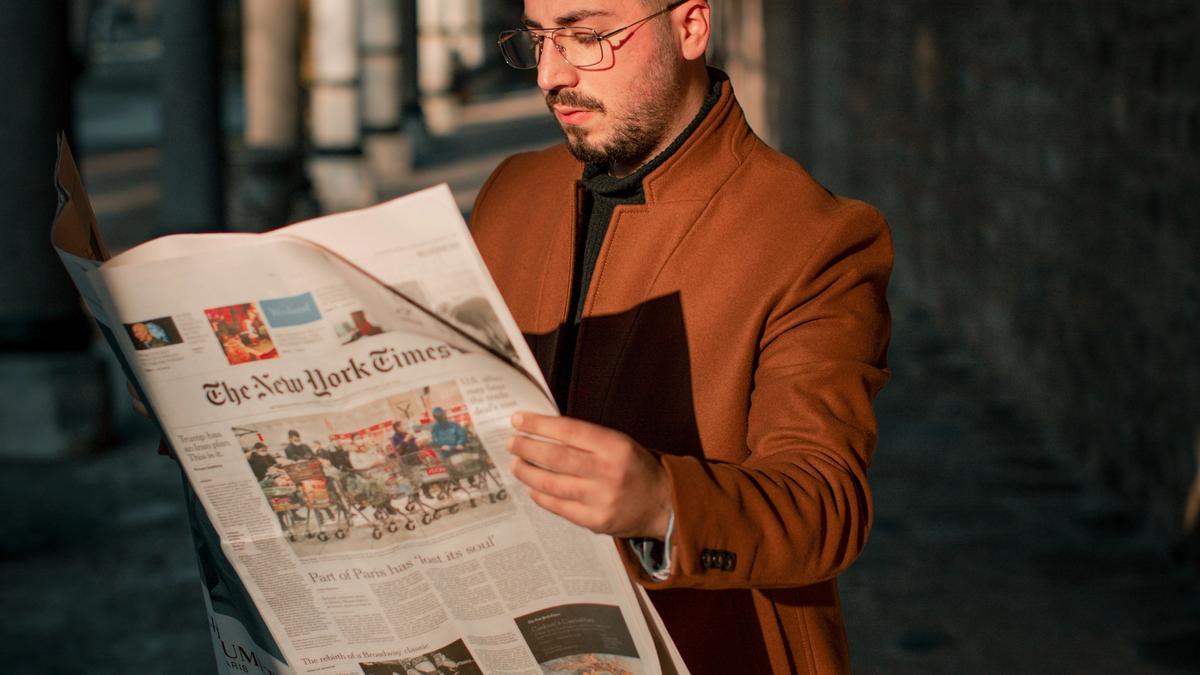 Illustrasjonsbilde av en ung mann med brun kåpe som står å leser en avis, tatt av Ömer Faruk Tokluoğlu fra Unsplash