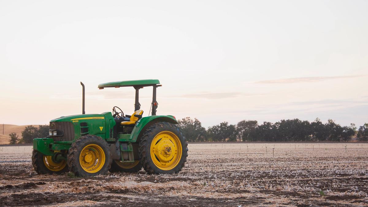 Grønn traktor som står på et jorde. Illustrasjonsbilde tatt av Nathan Lugo fra Unsplash