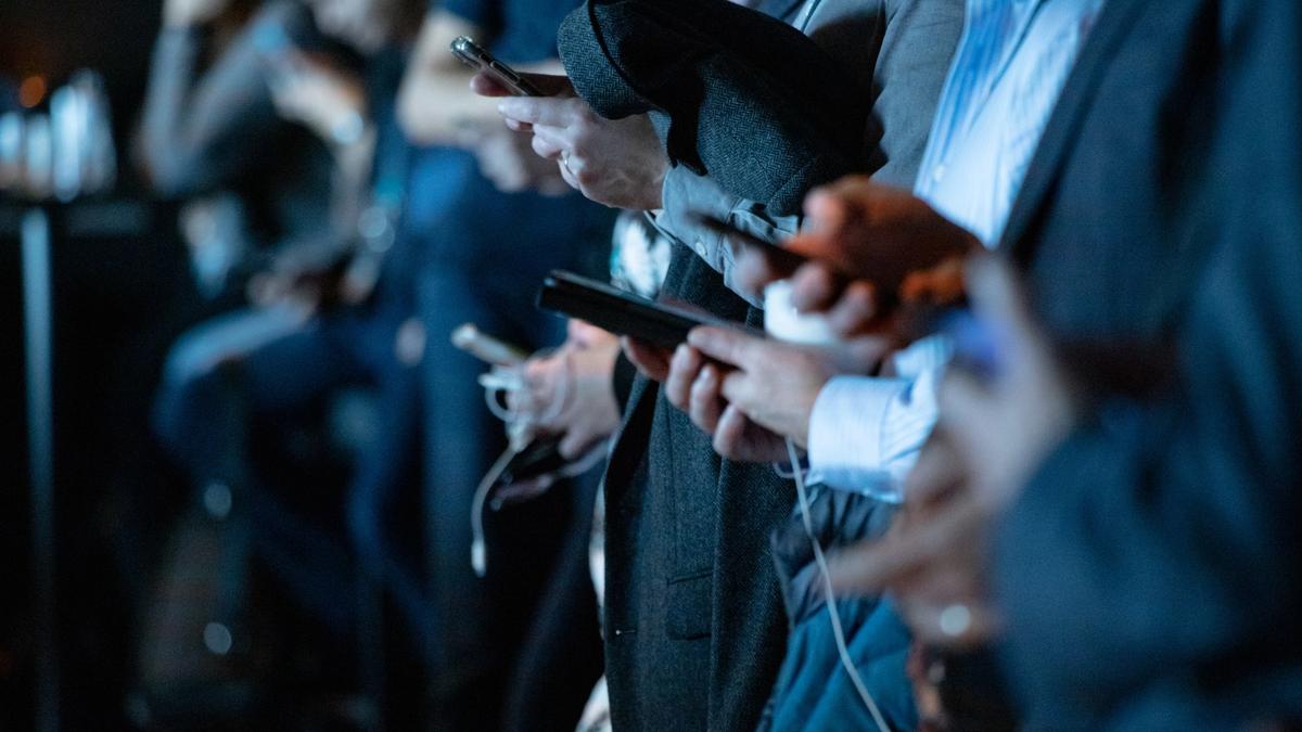 Illustrasjonsbilde av personer mange personer på rad i mørke dresser som holder mobilene sine tatt av camilo jimenez fra Unsplash