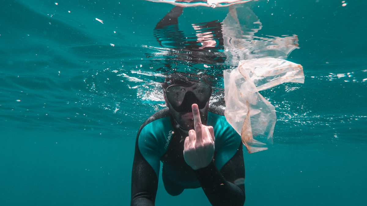 Bilde av en som dykker i havoverflaten, og viser fingeren til en plastpose i vannet.