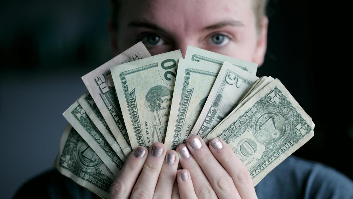 Person holding dollar bills in front of their face