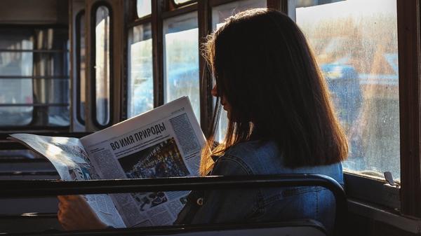 Illustrasjonsbilde av en kvinne som leser avisen på en buss tatt av Artem fra Pexels