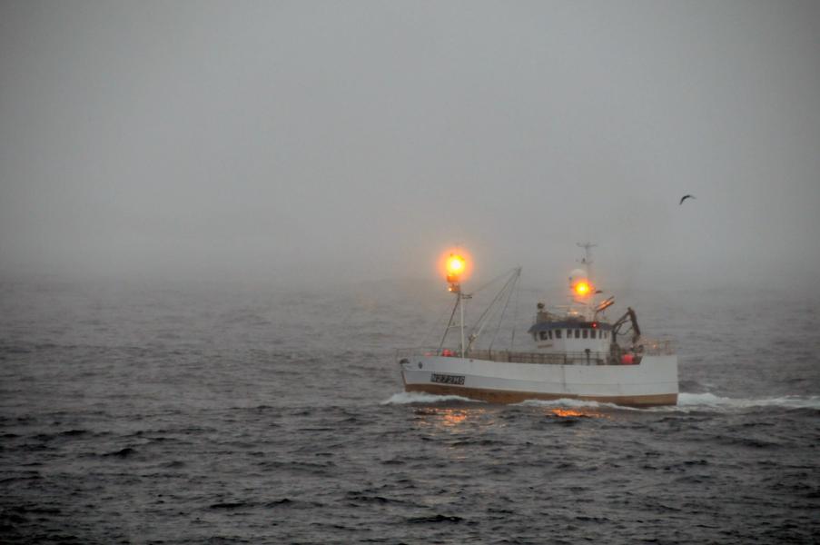 Liten fiskebåt i tre, langt til havs i skumring med lysende lanterner
