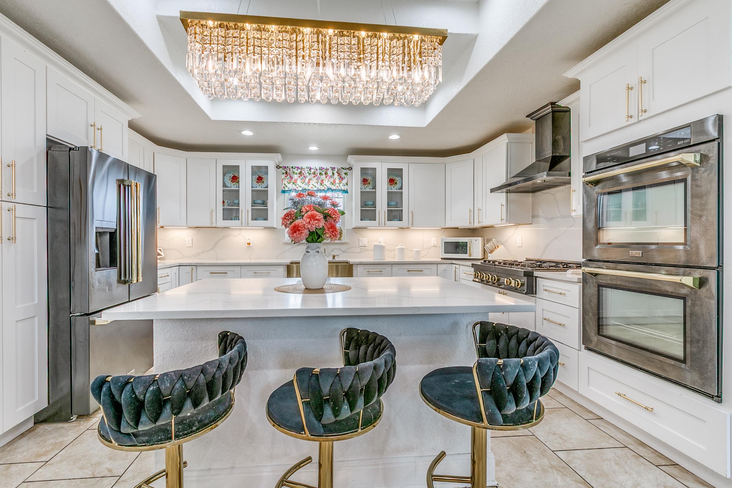 White kitchen with quartz island, gold hardware, crystal chandelier, and floral accents in a San Antonio home