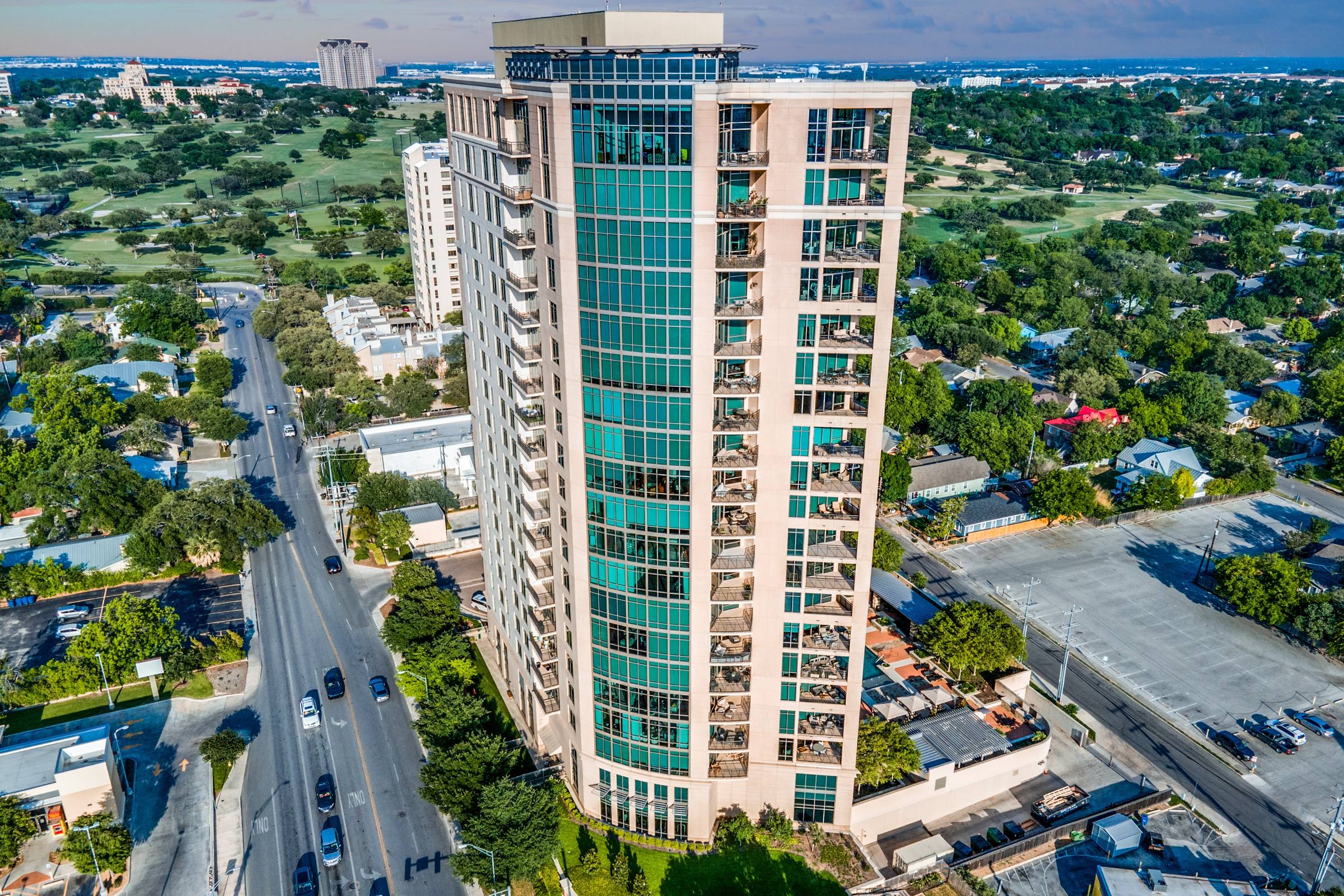 Aerial drone photograph of a luxury glass high-rise apartment tower with golf course views and tree-lined neighborhood in San Antonio, Texas