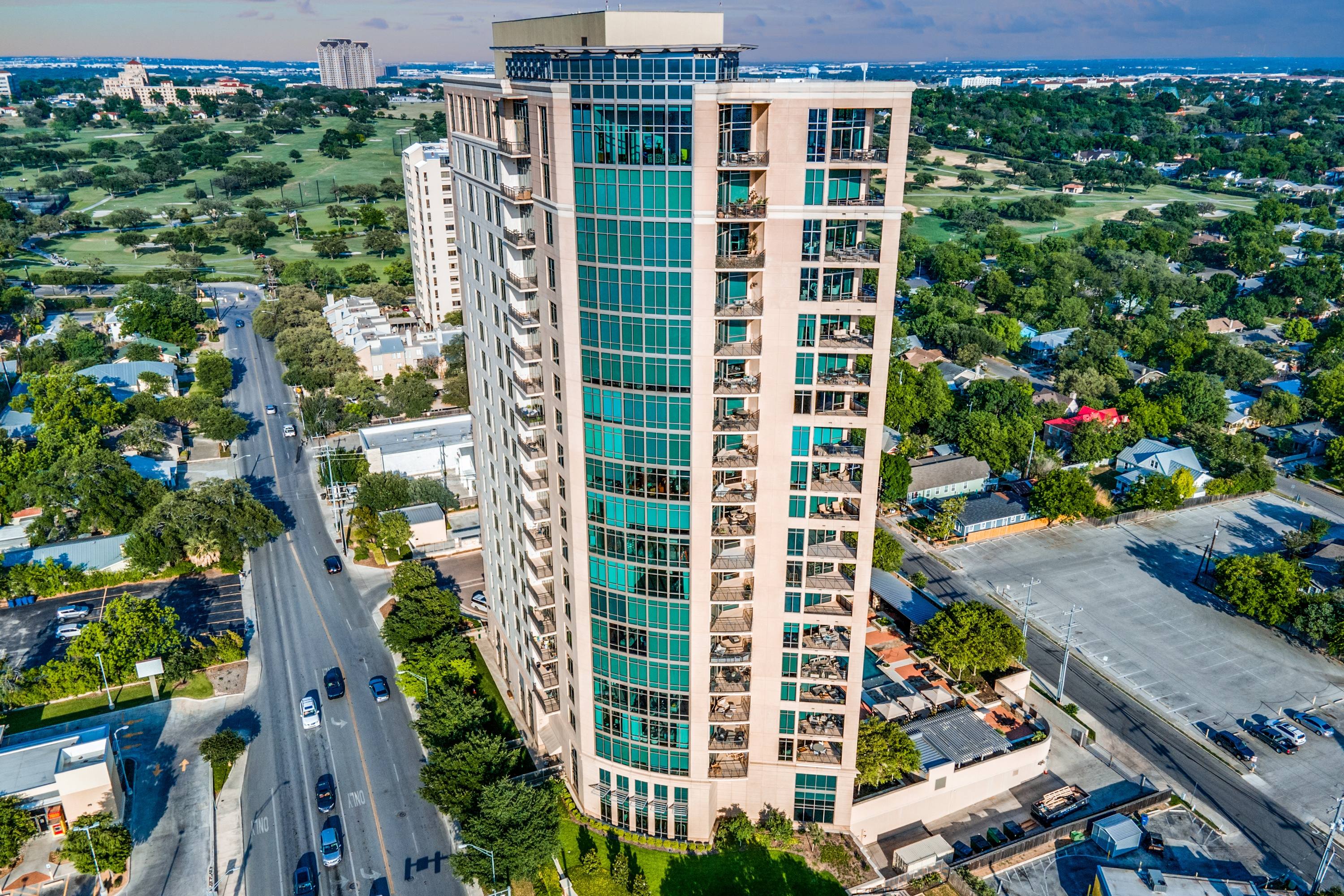 Aerial drone photograph of a luxury glass high-rise apartment tower with golf course views and tree-lined neighborhood in San Antonio, Texas