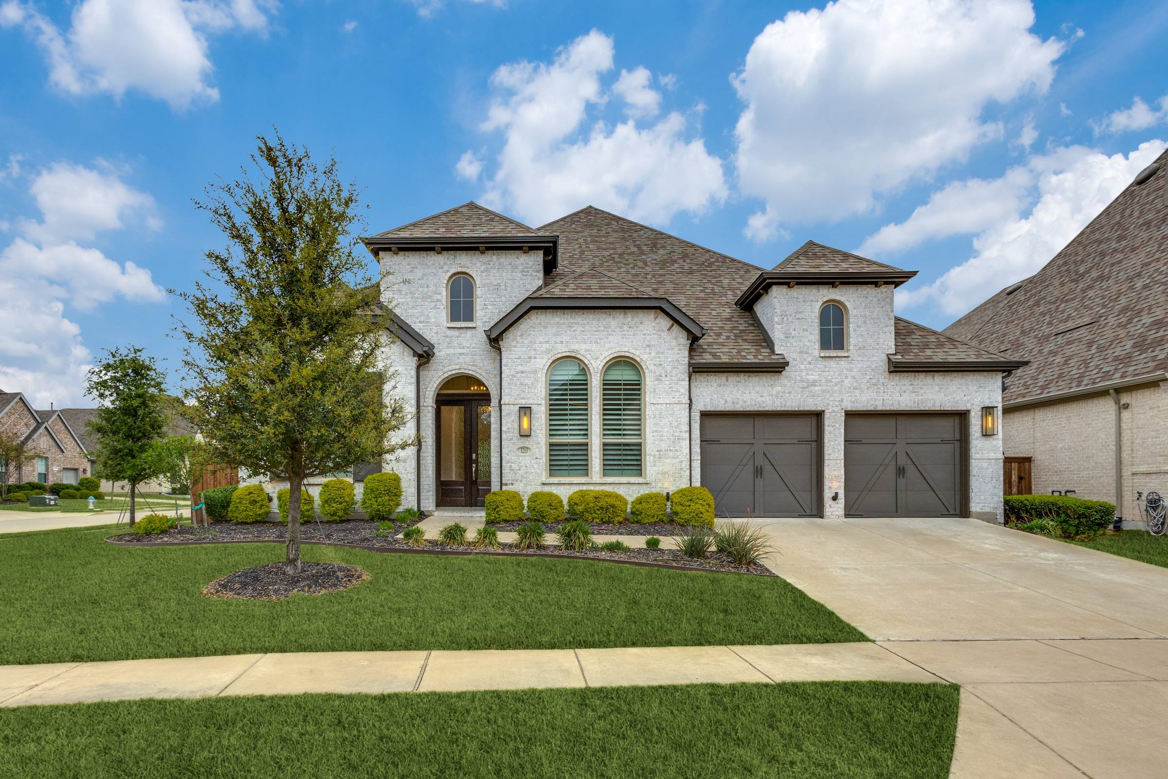 Front exterior of a white brick two-story single-family home with two-car garage and manicured lawn in Celina, Texas