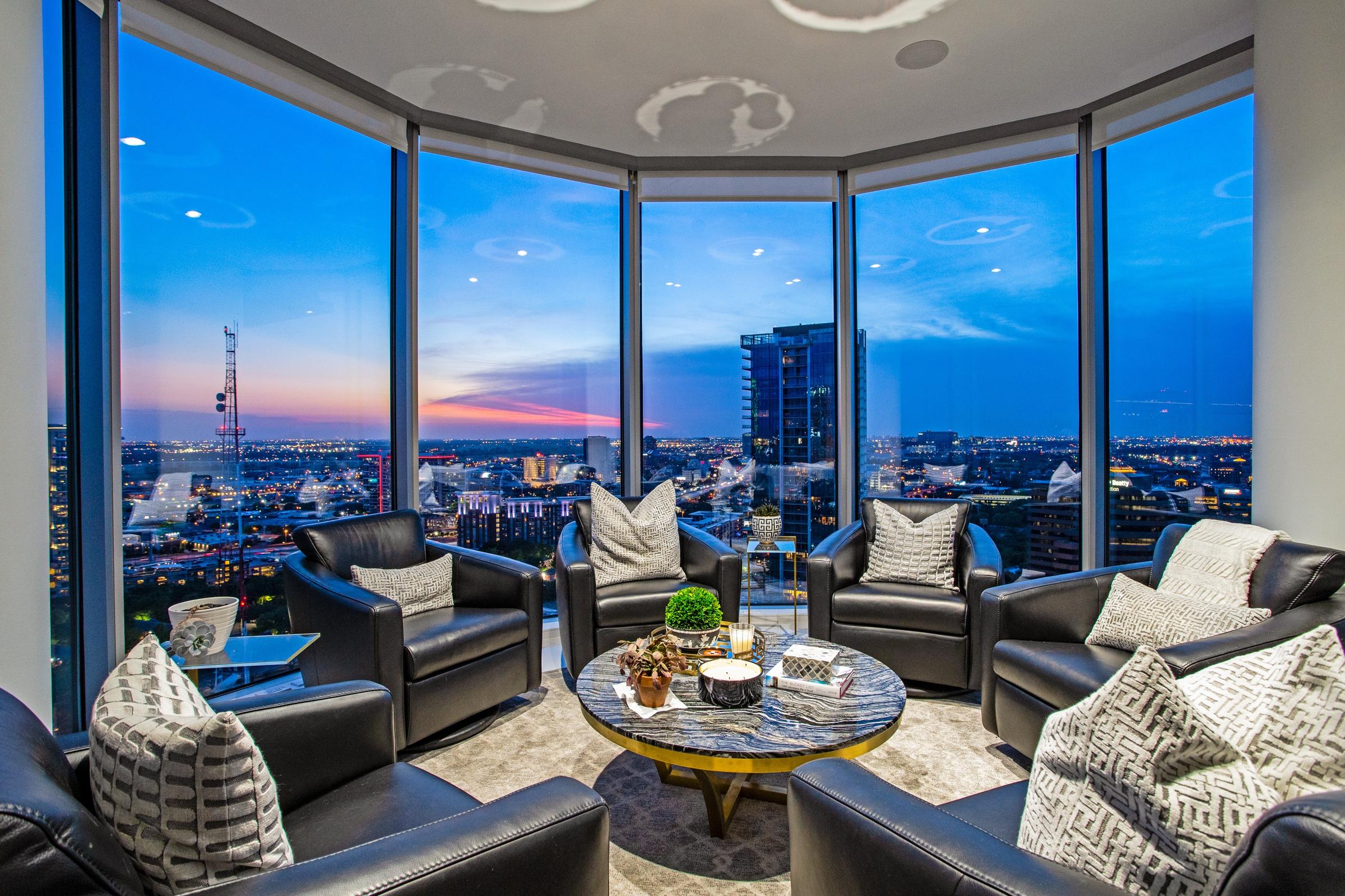 Luxury high-rise apartment lounge with floor-to-ceiling curved windows overlooking the Downtown Dallas skyline at sunset in Dallas, Texas
