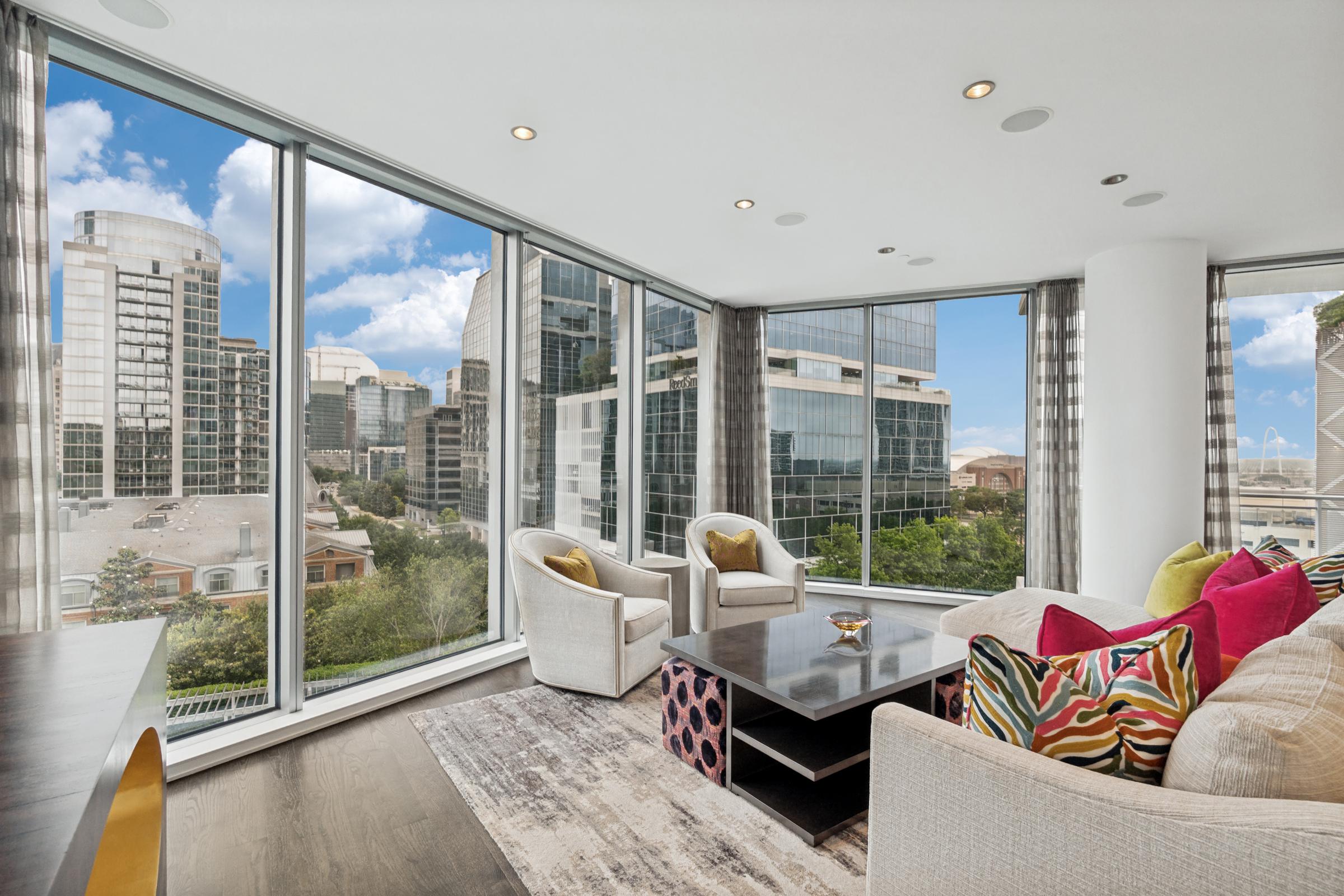 High-rise condo living room with colorful throw pillows and corner windows overlooking the downtown Dallas skyline