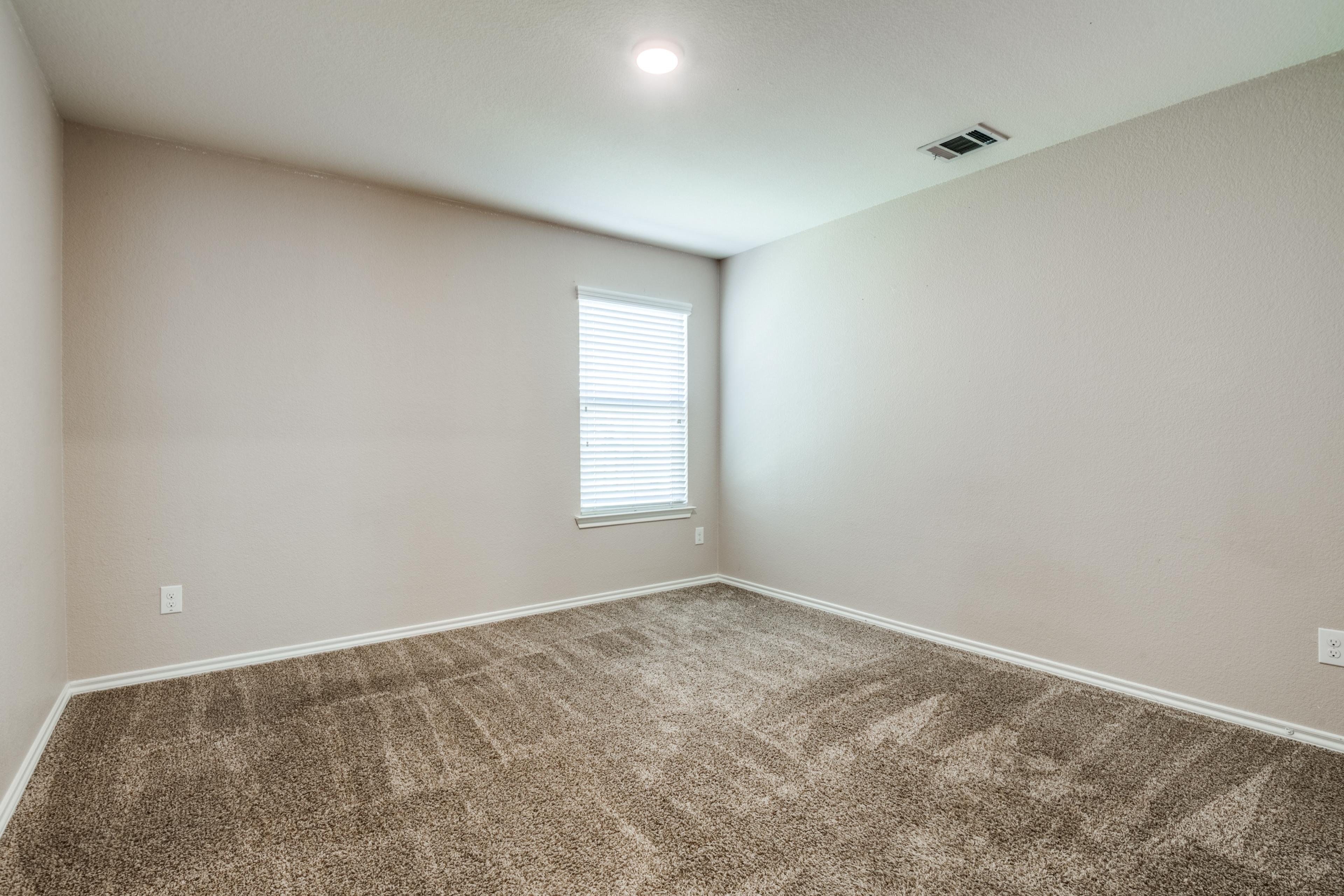 Vacant carpeted bedroom with single window in a Royse City, Texas rental property before virtual staging
