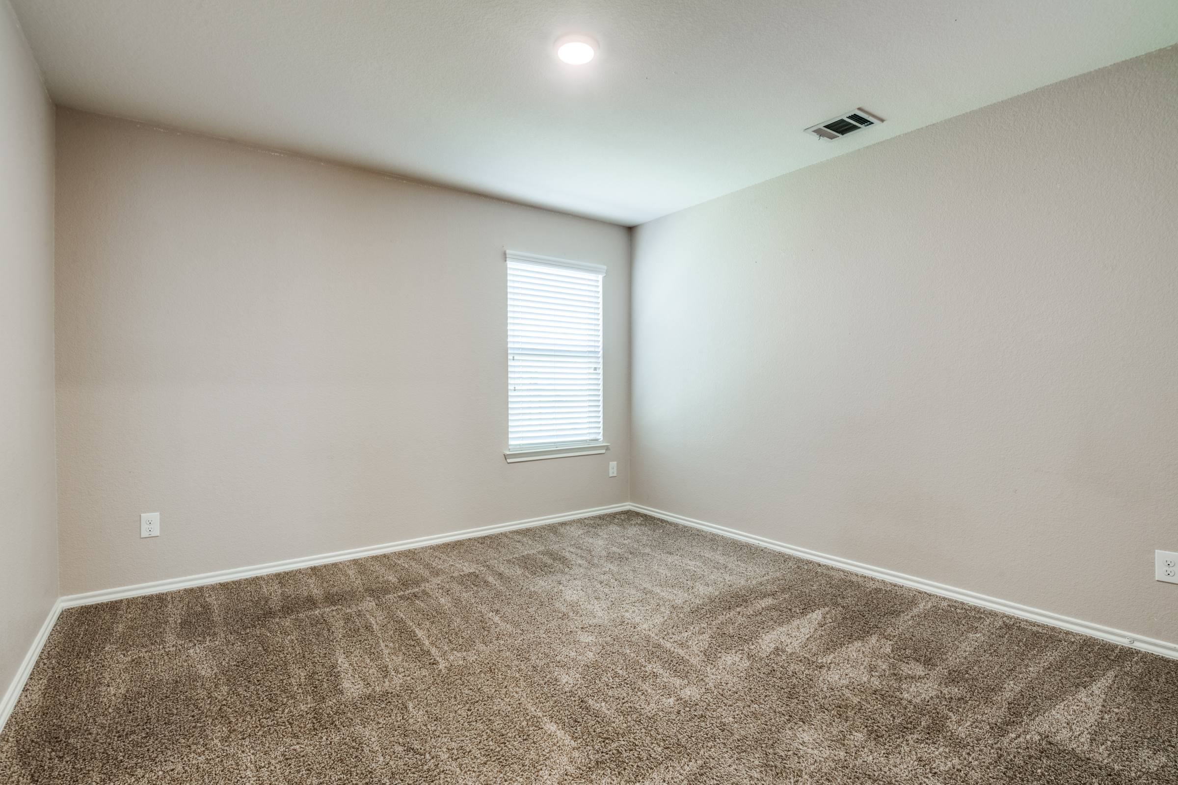 Vacant carpeted bedroom with single window in a Royse City, Texas rental property before virtual staging
