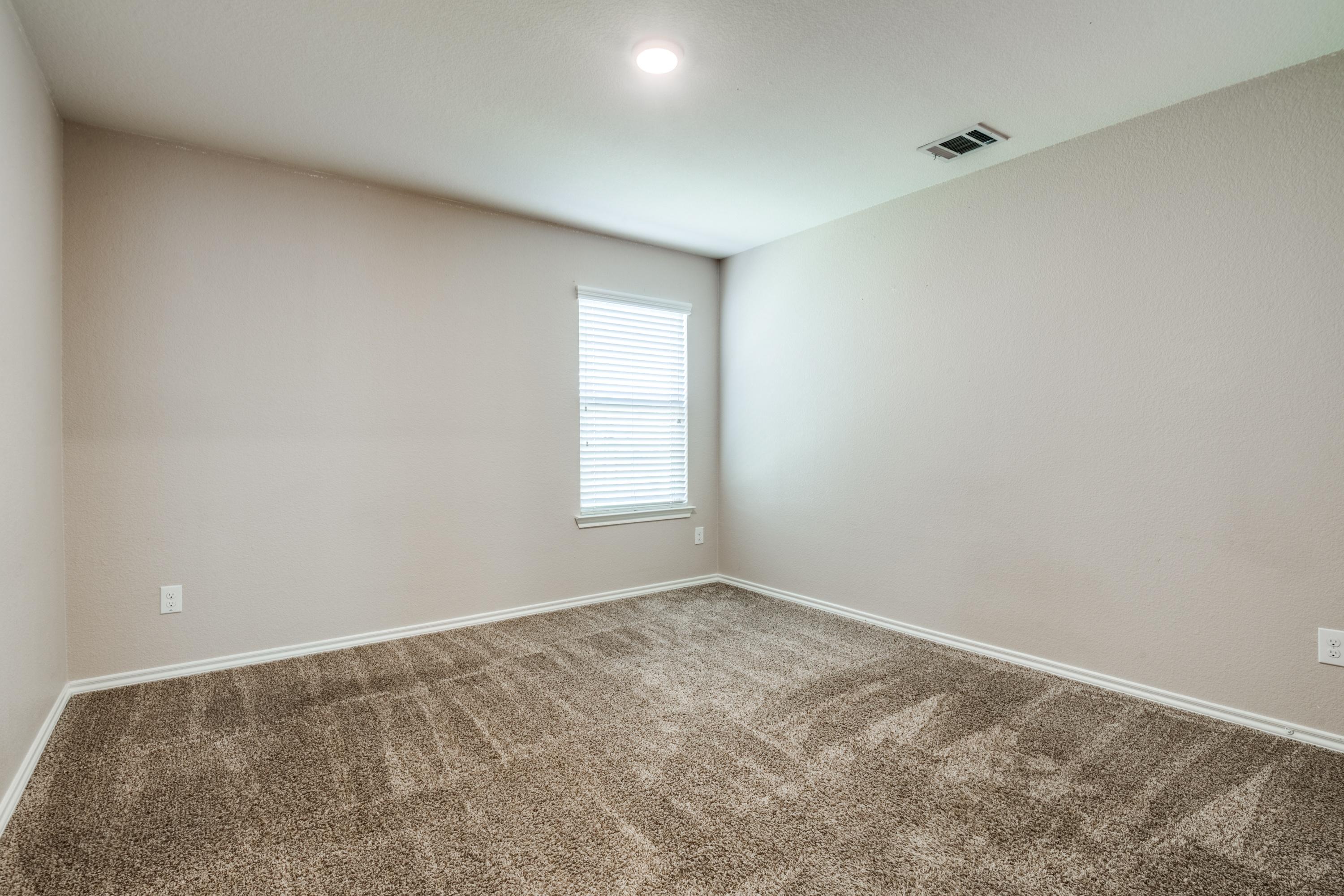 Vacant carpeted bedroom with single window in a Royse City, Texas rental property before virtual staging