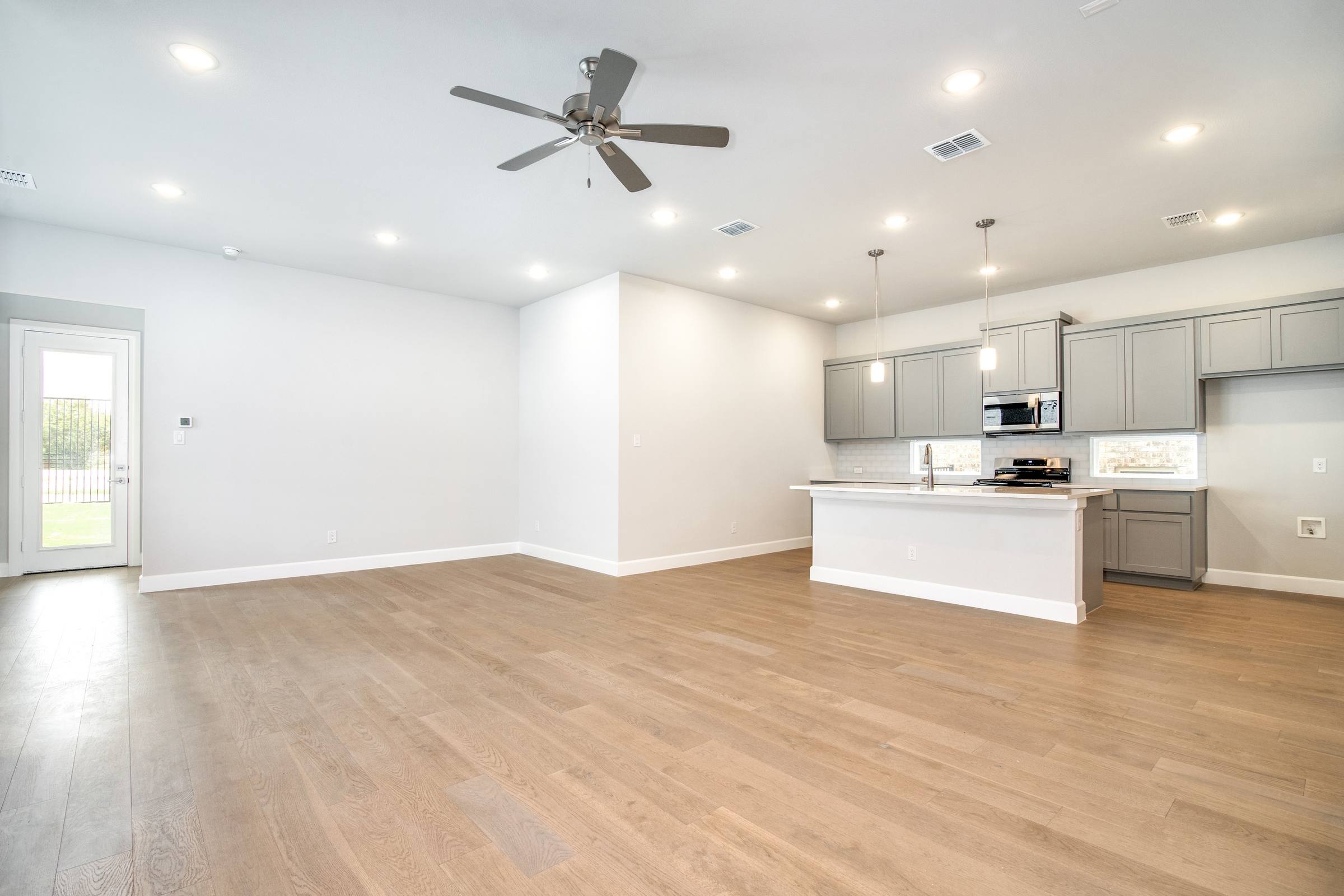Empty open-concept kitchen and living area with gray cabinets and hardwood floors before virtual staging in Heath, Texas