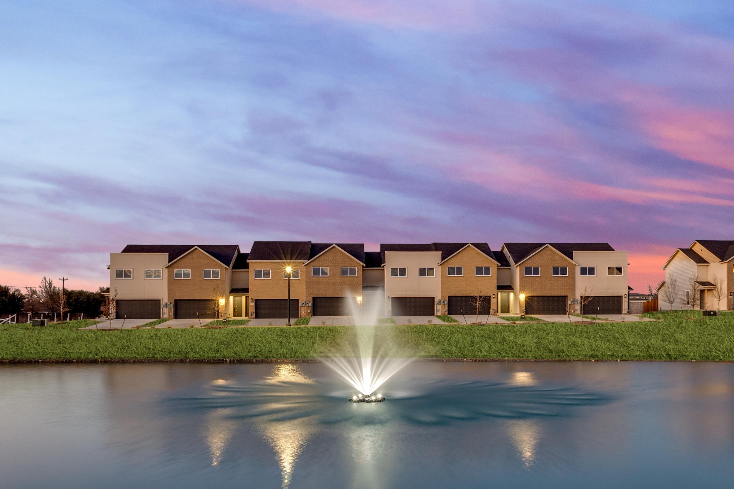 Row of townhomes with pond fountain reflecting a vibrant pink and purple twilight sky in Melissa, Texas