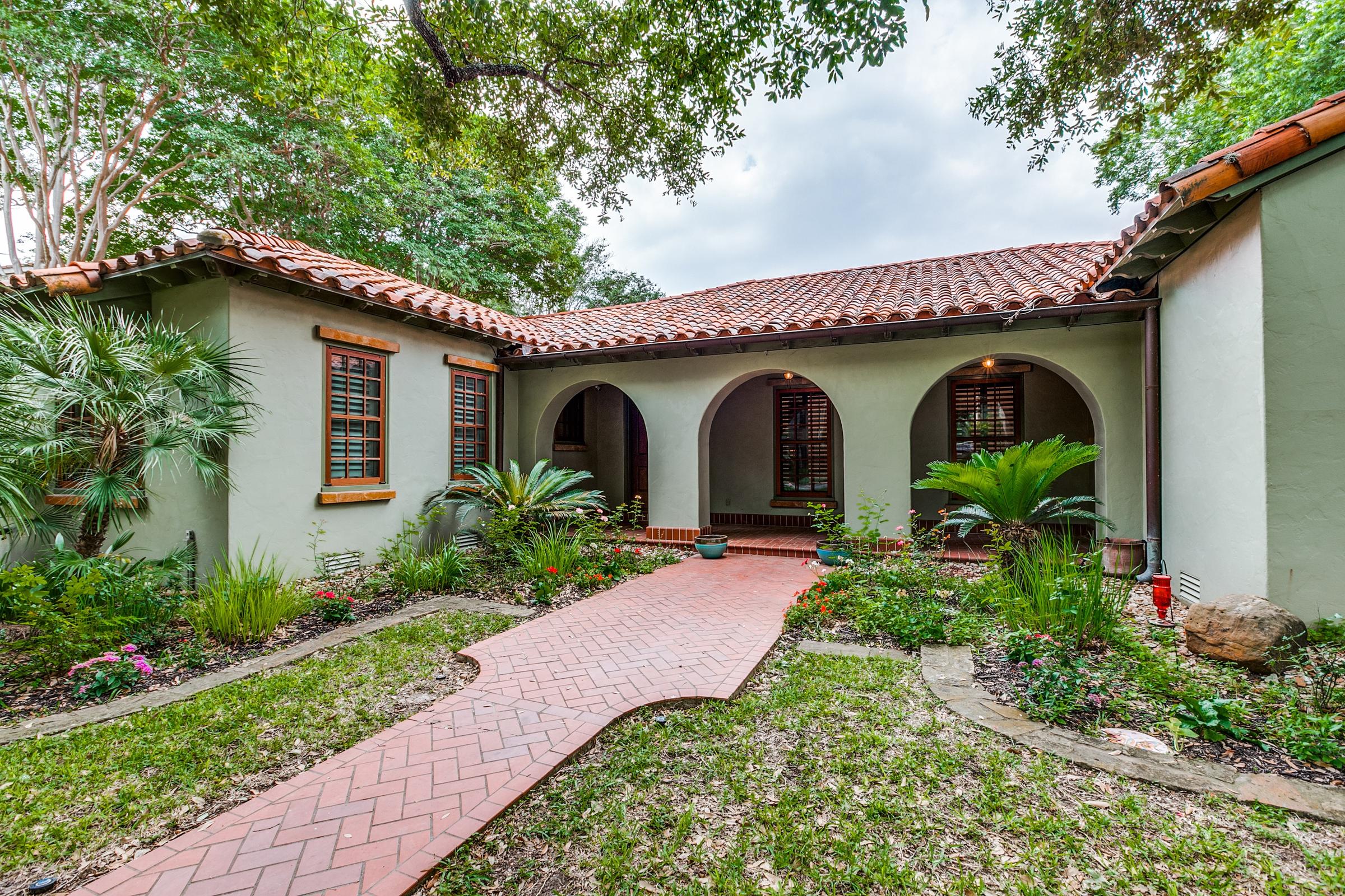 Professional real estate photography of a Spanish-style villa with clay tile roof, arched entryway, and brick walkway in Alamo Heights, Texas