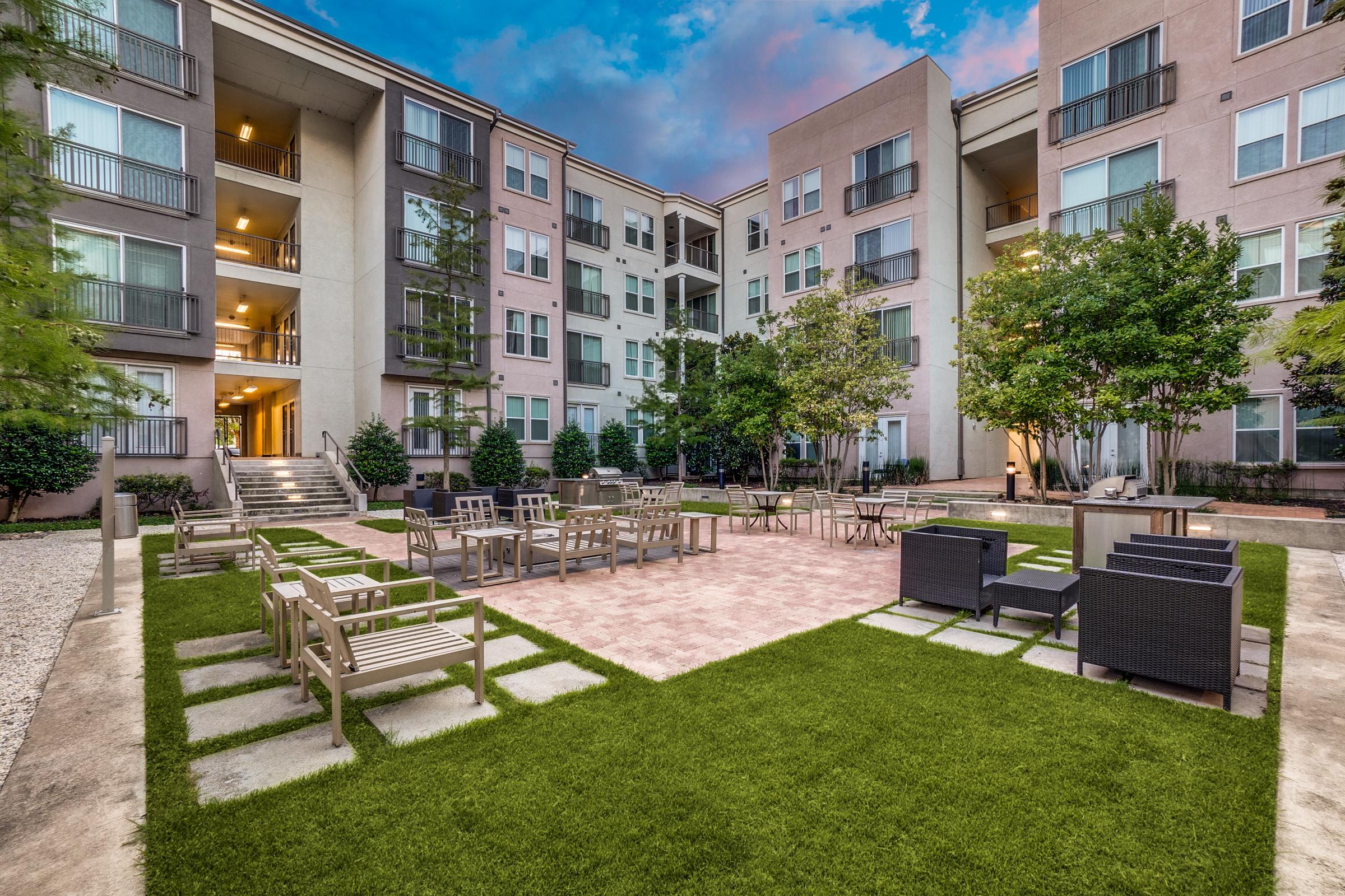 Outdoor courtyard seating area with benches and landscaped turf at twilight at an apartment community in Garland, Texas