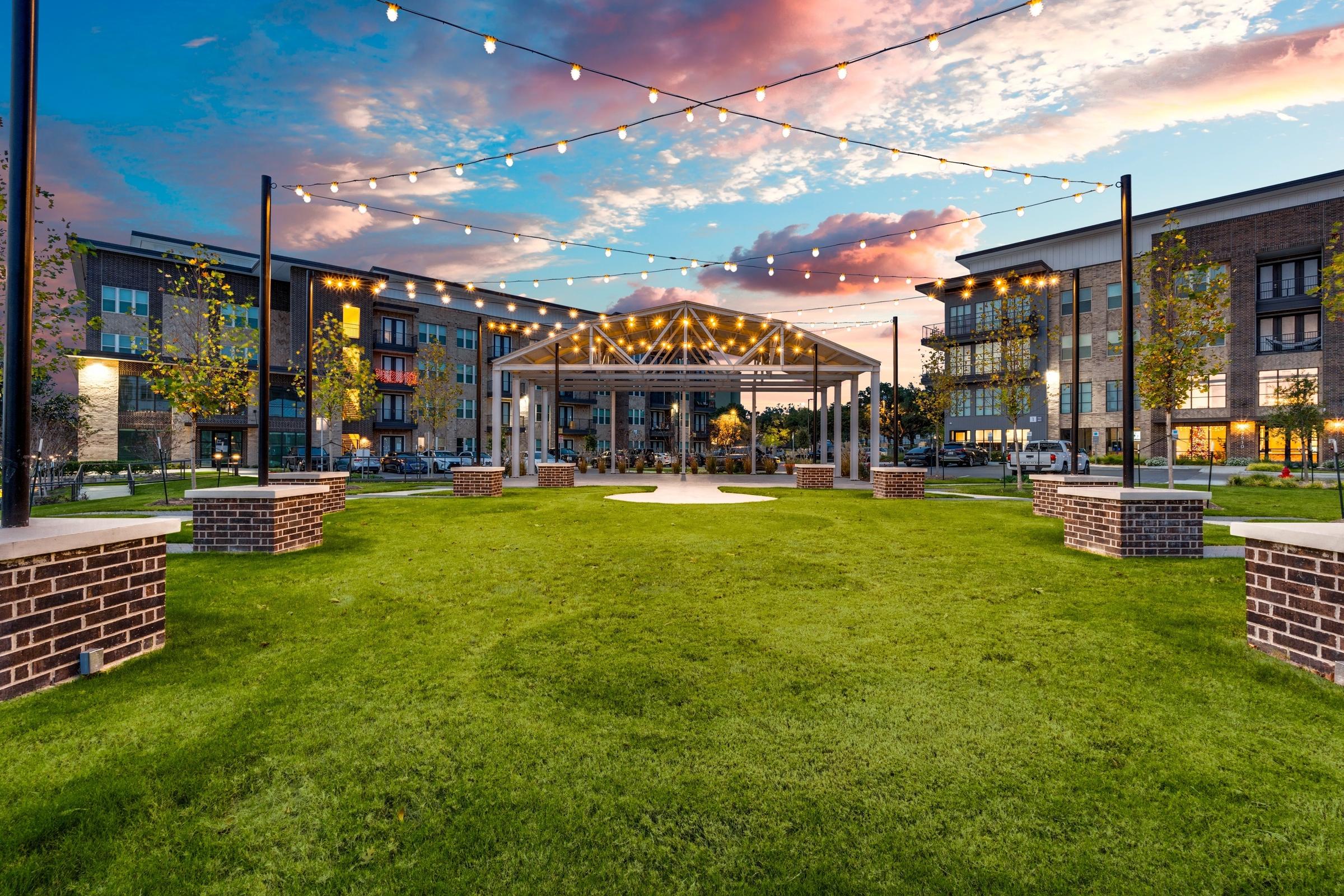 Multifamily apartment community courtyard with string lights, pavilion, and manicured lawn at twilight in San Antonio, Texas