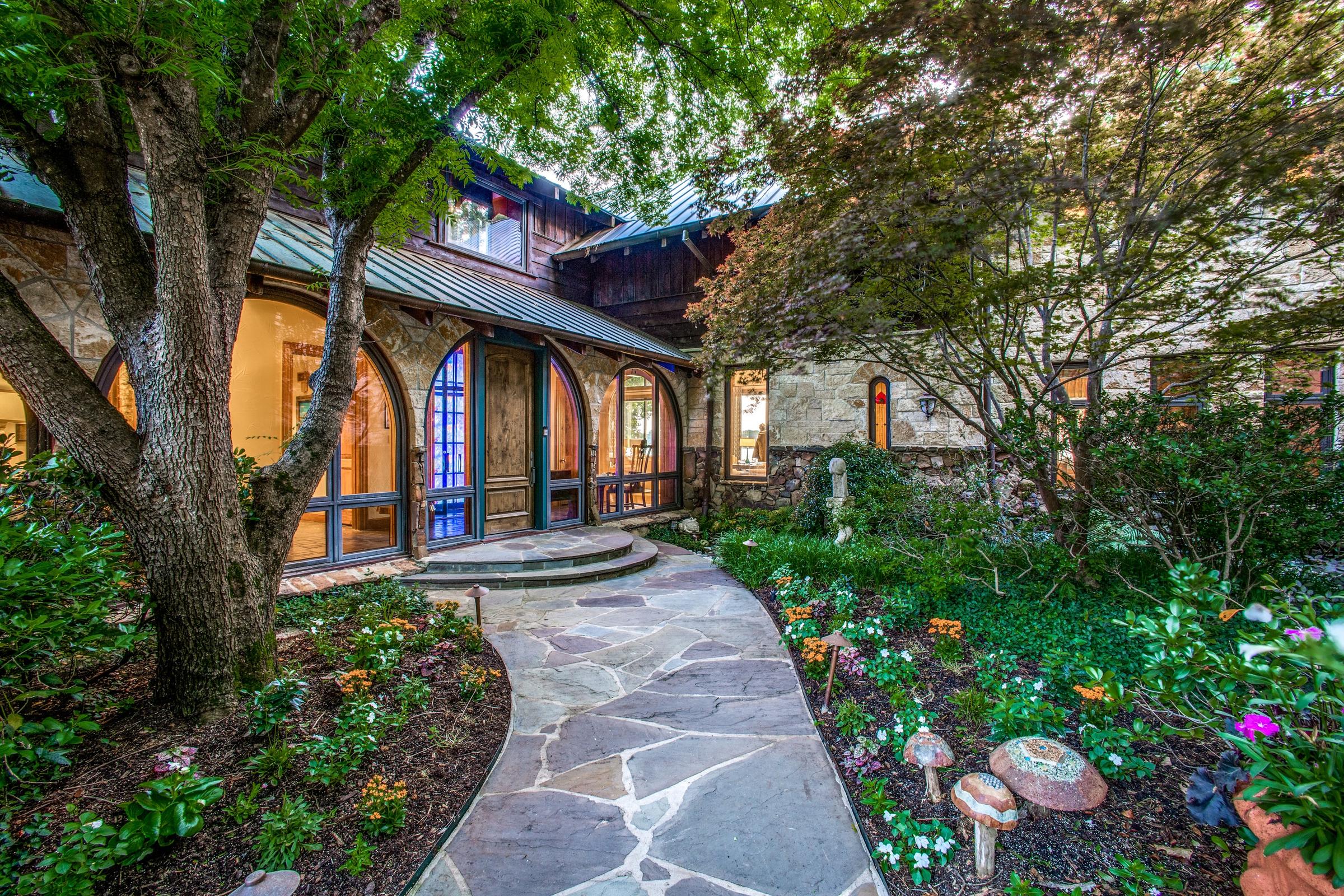 Lush backyard courtyard with stone pathway leading to arched glass doors surrounded by mature trees and gardens in Malakoff, Texas