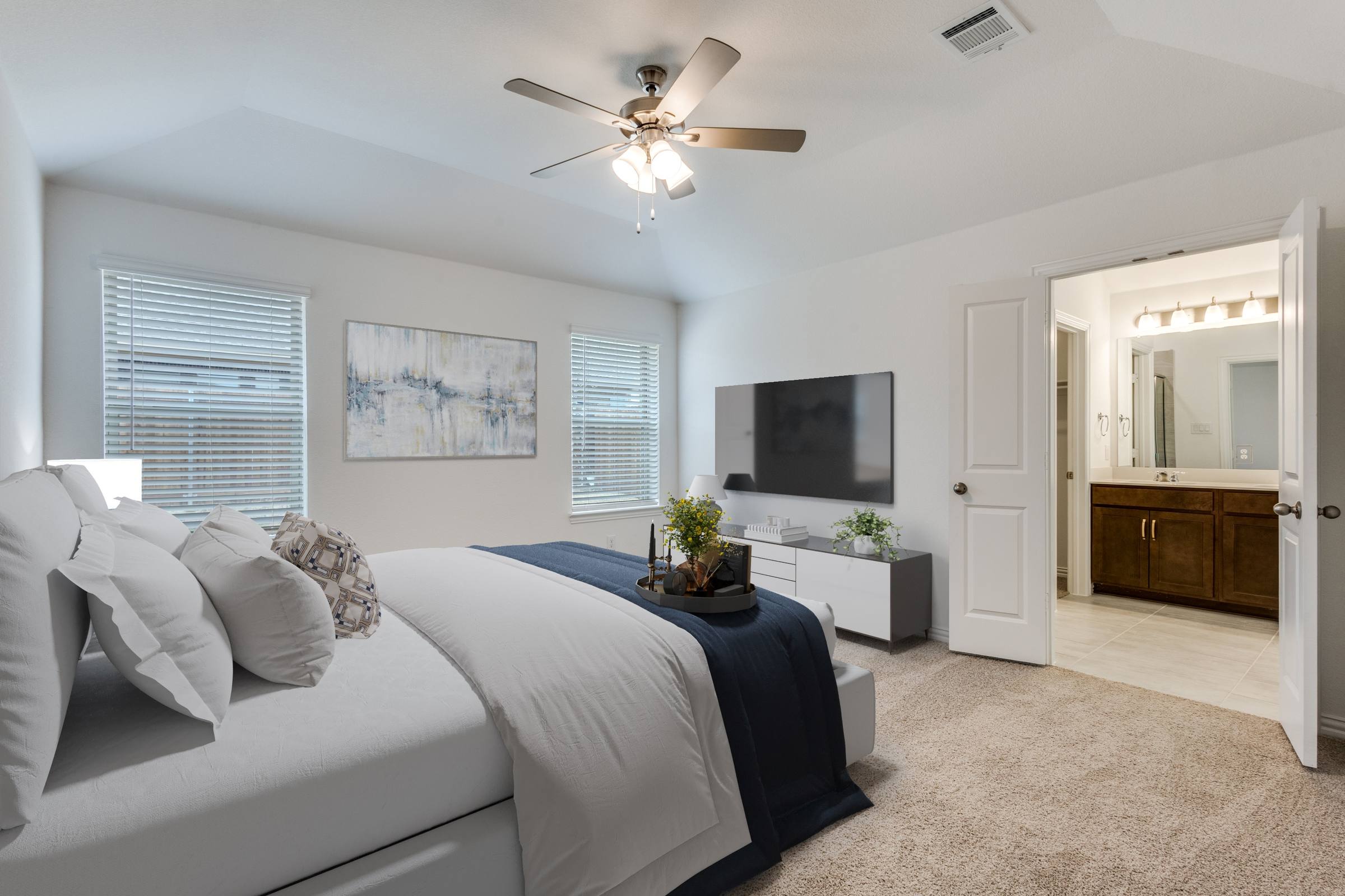 Virtually staged master bedroom with king bed, navy throw, wall-mounted TV, and media console in Anna, Texas