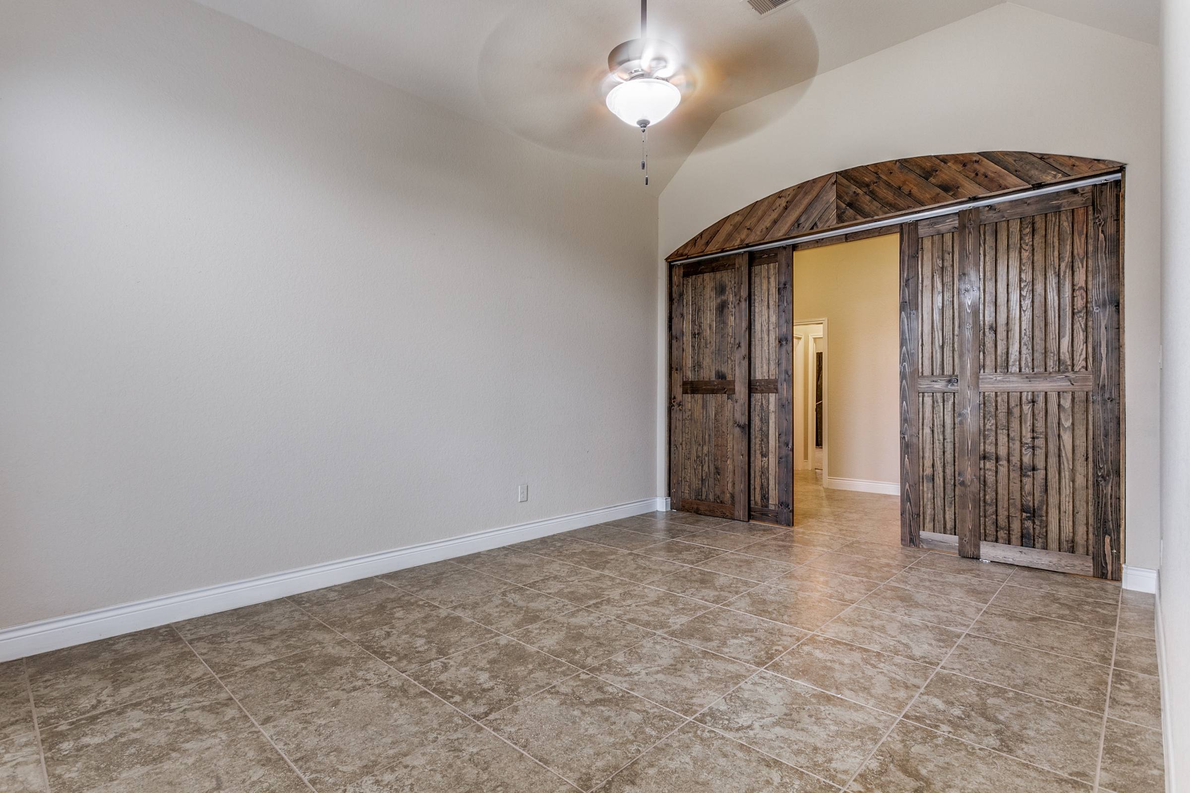 Empty dining room with tile floors and rustic arched barn doors before virtual staging in New Braunfels, Texas
