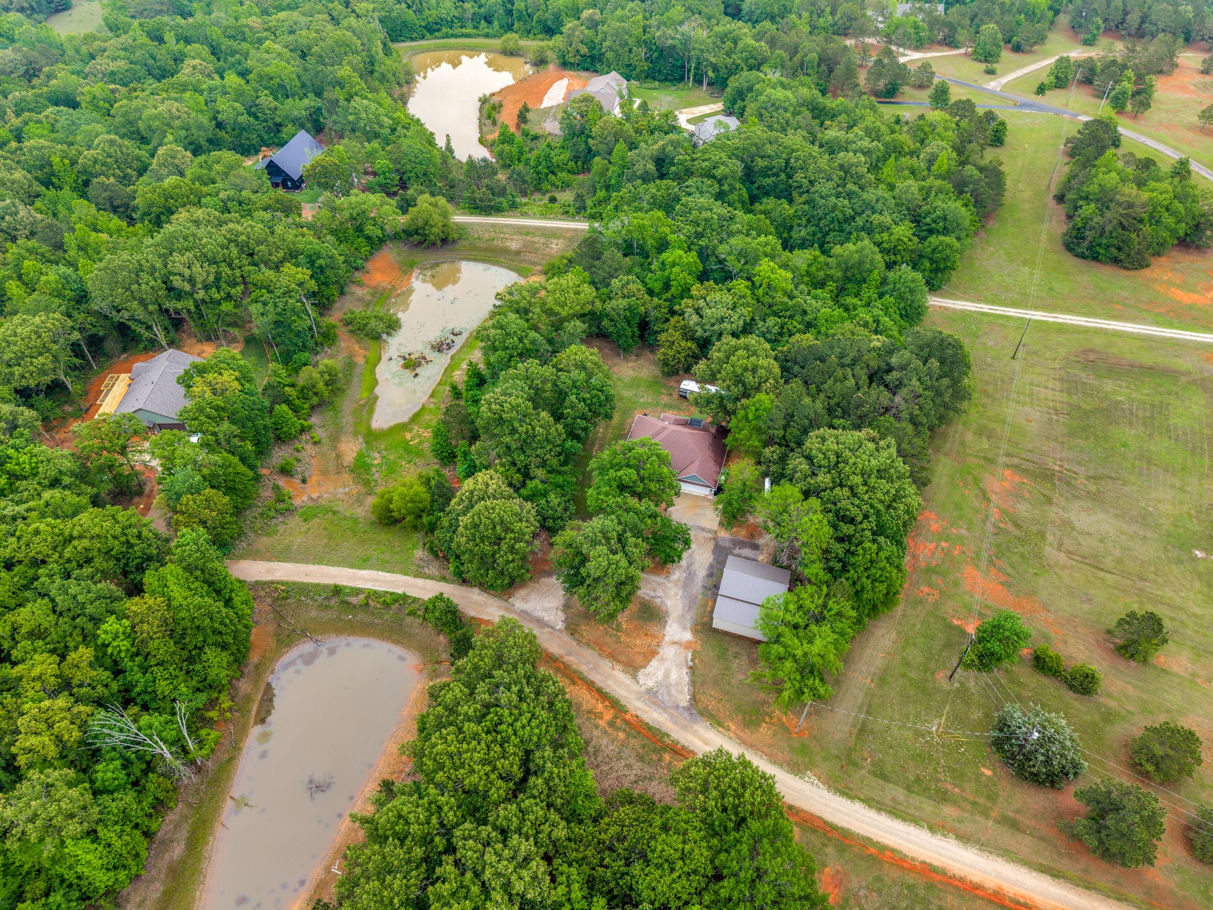 Aerial view of a rural Thedford, TX estate with a main house, outbuildings, multiple stock ponds, and winding gravel drive — shown with unenhanced seasonal grass color (before Aerial Green Grass treatment).