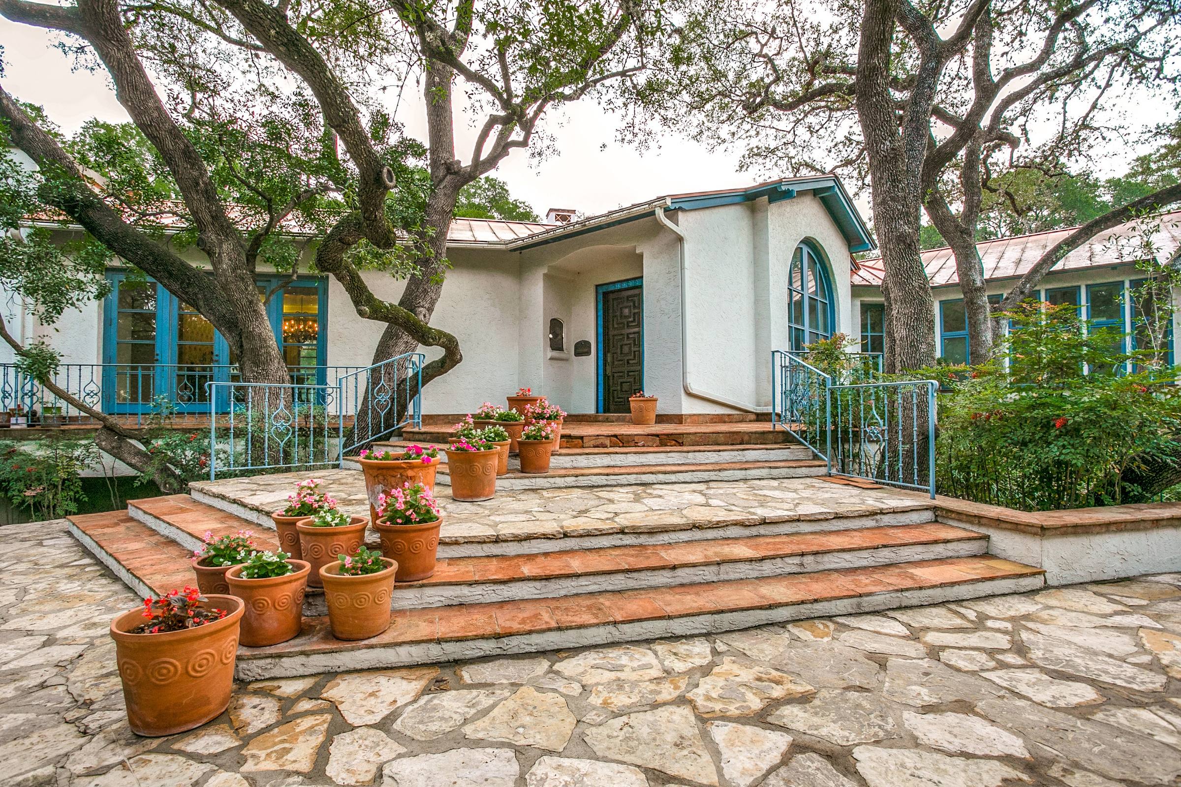 Spanish Mediterranean style front entry with stone steps, terra cotta planters and turquoise-trimmed windows in San Antonio, Texas
