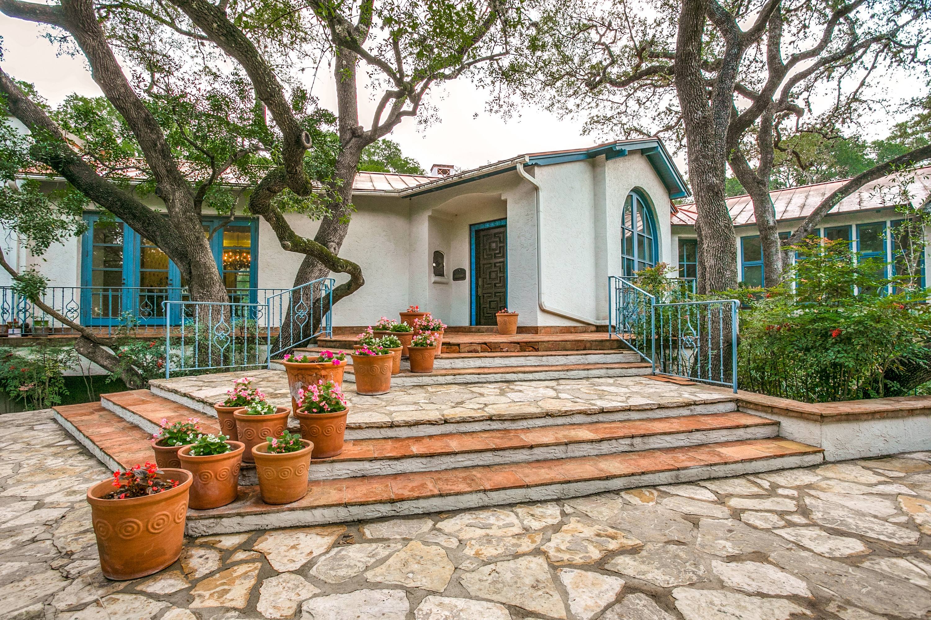 Spanish Mediterranean style front entry with stone steps, terra cotta planters and turquoise-trimmed windows in San Antonio, Texas