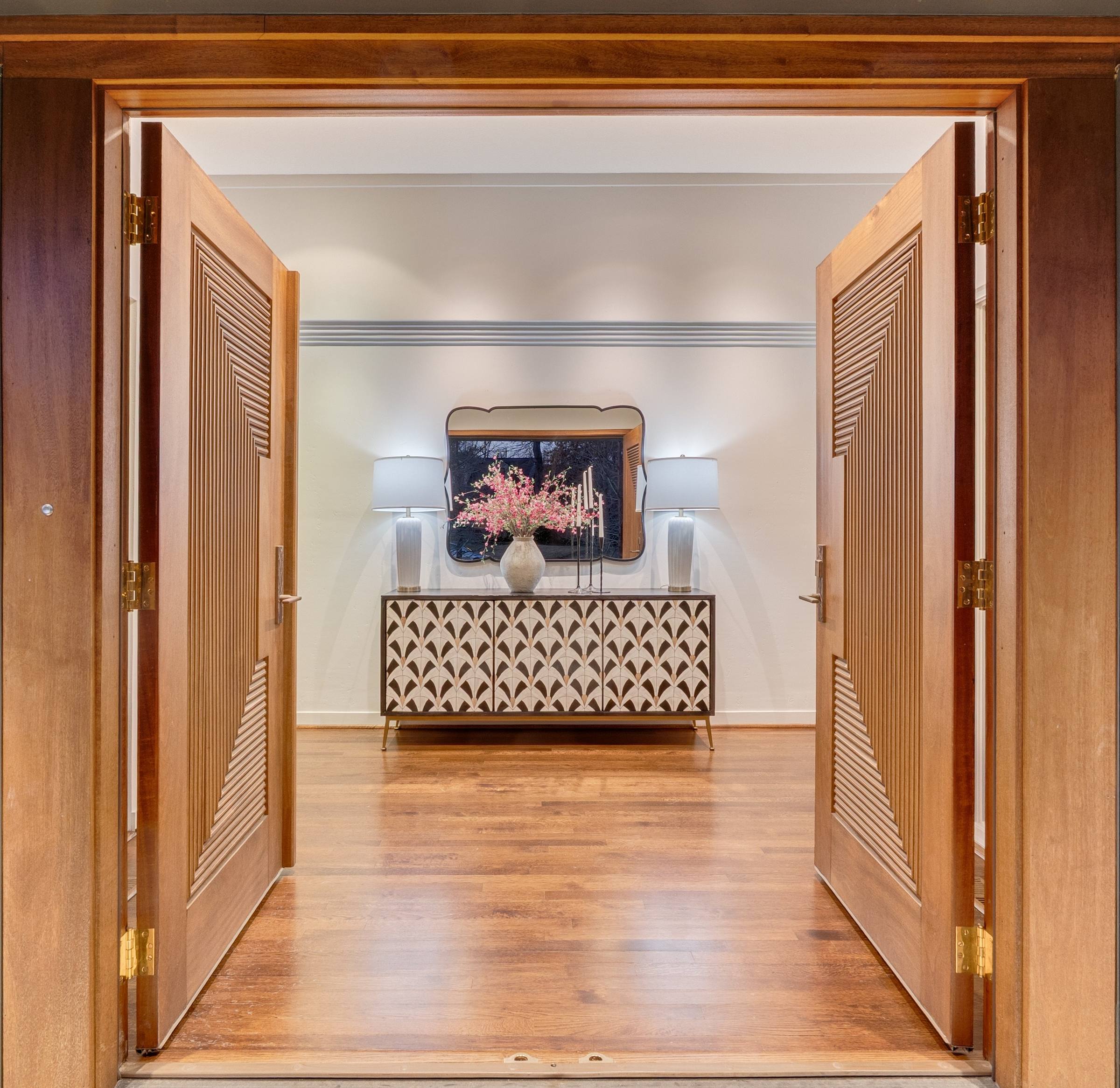 Grand wooden double doors opening to an elegant foyer with cherry blossom arrangement in a Katy, Texas luxury home