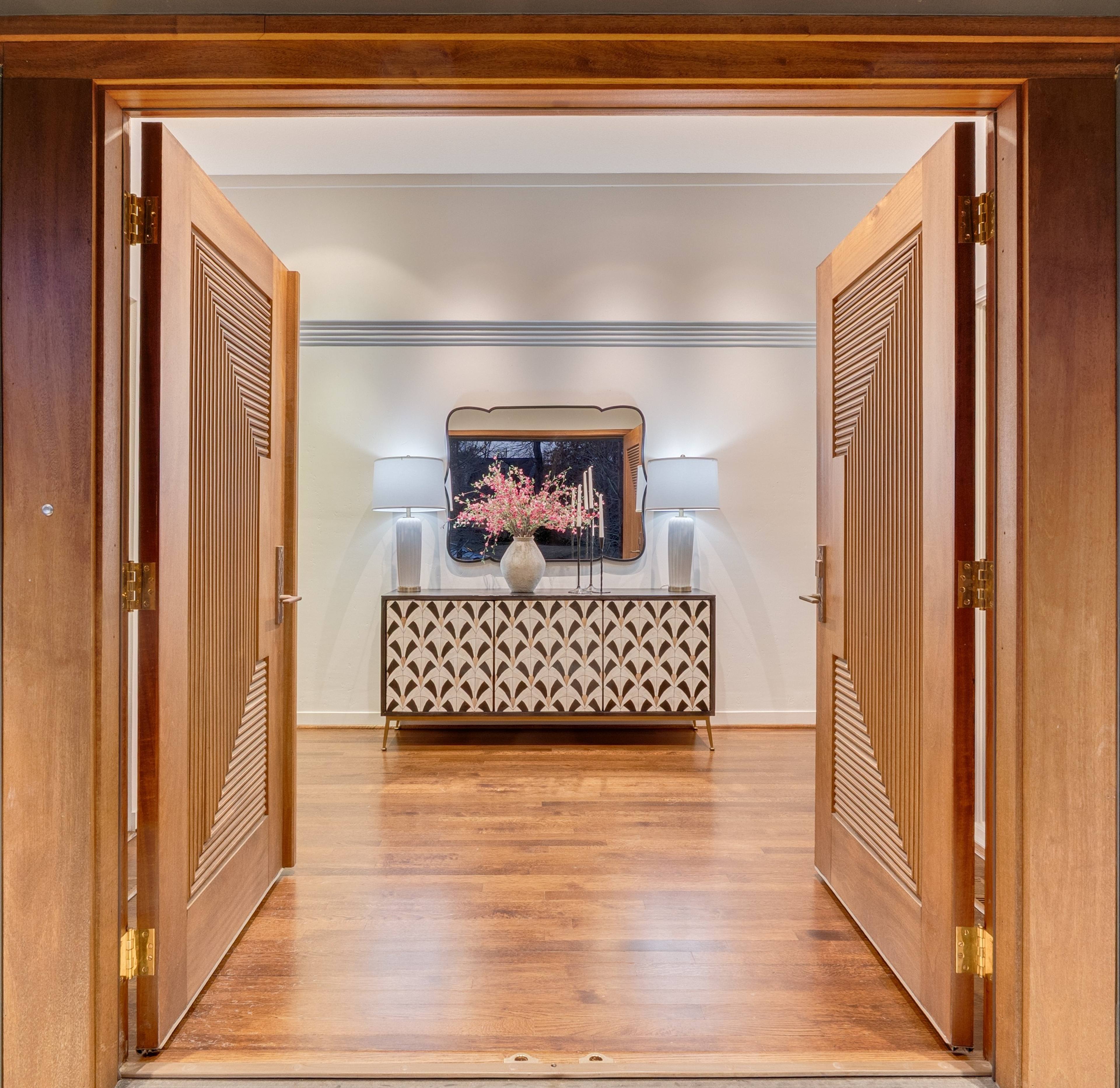 Grand wooden double doors opening to an elegant foyer with cherry blossom arrangement in a Katy, Texas luxury home