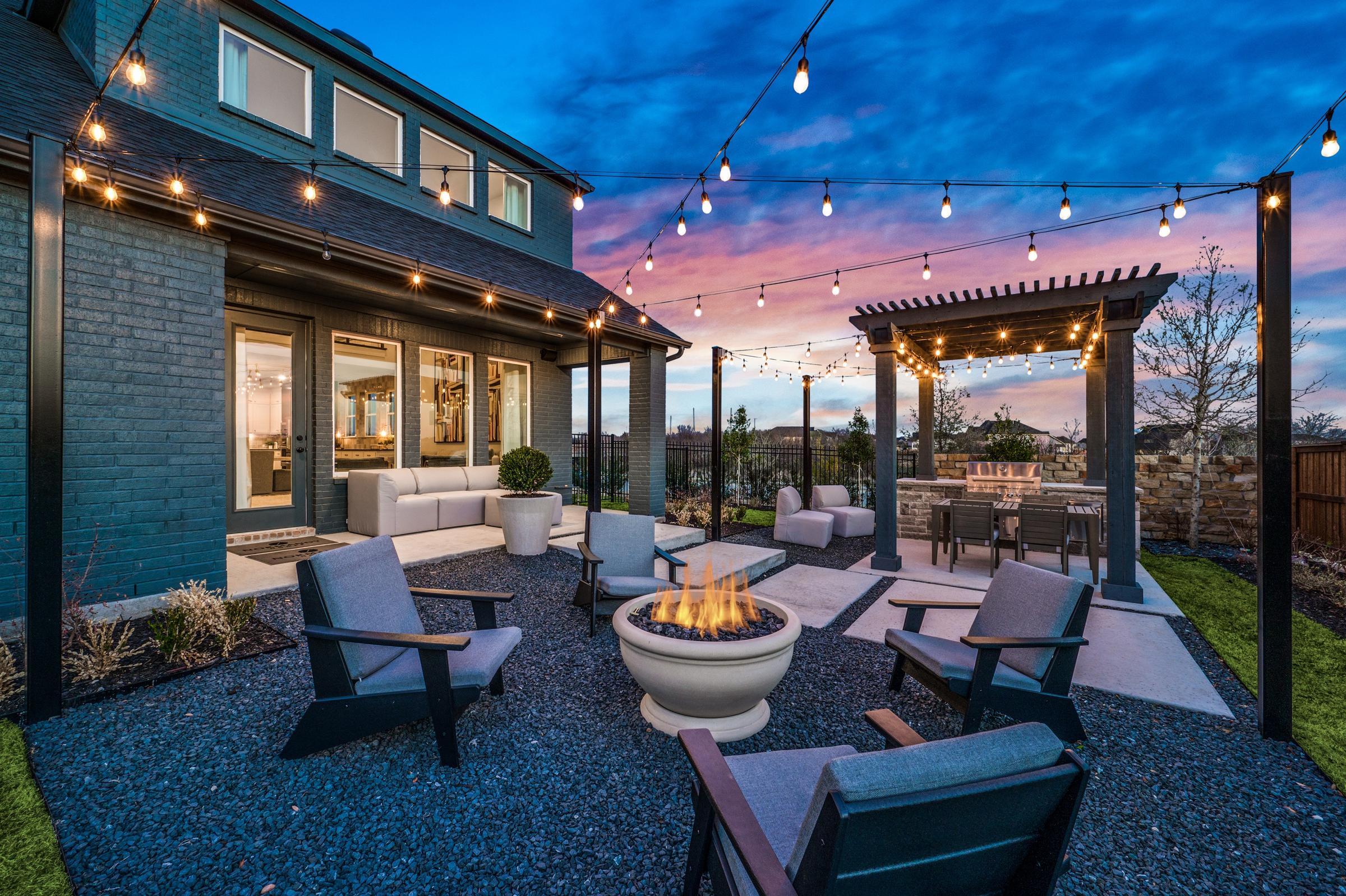 Luxury backyard at twilight with pergola, fire pit lounge, string lights, and outdoor kitchen in Prosper, Texas