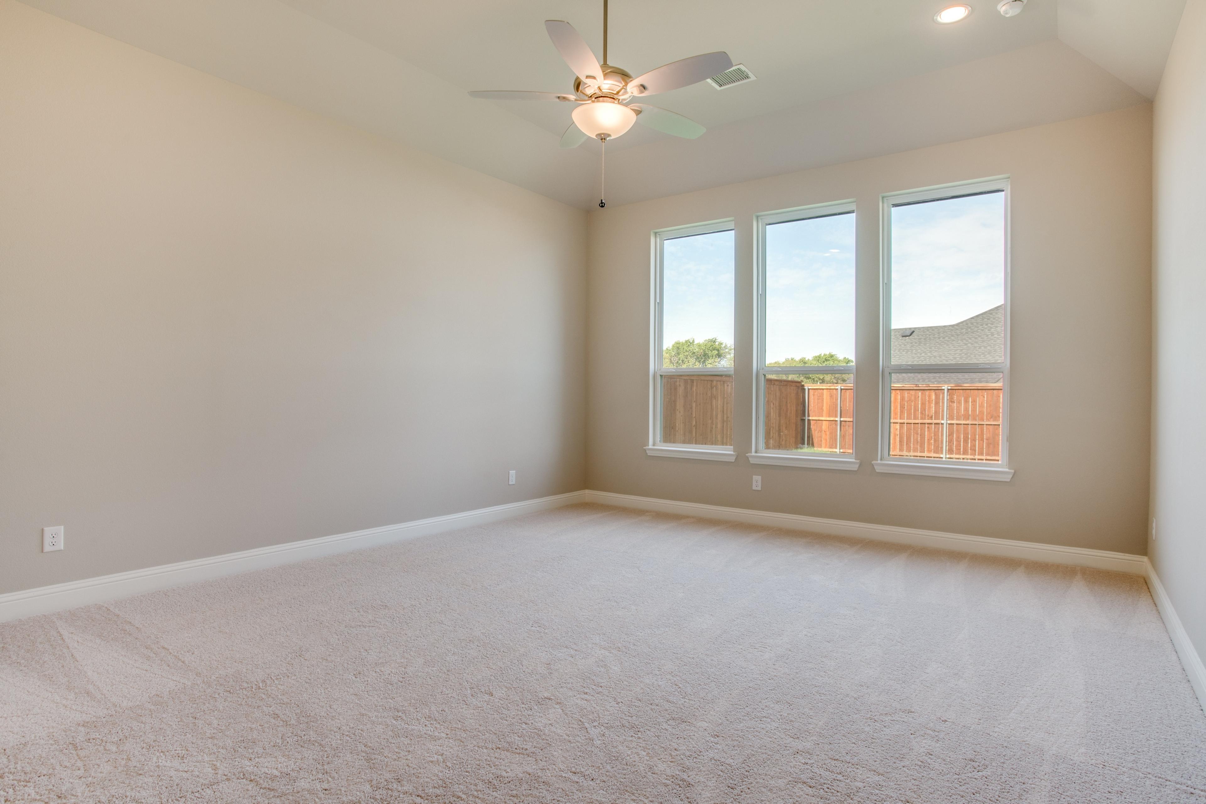 Empty master bedroom with vaulted ceiling and ceiling fan before virtual staging in new construction home in Celina, Texas