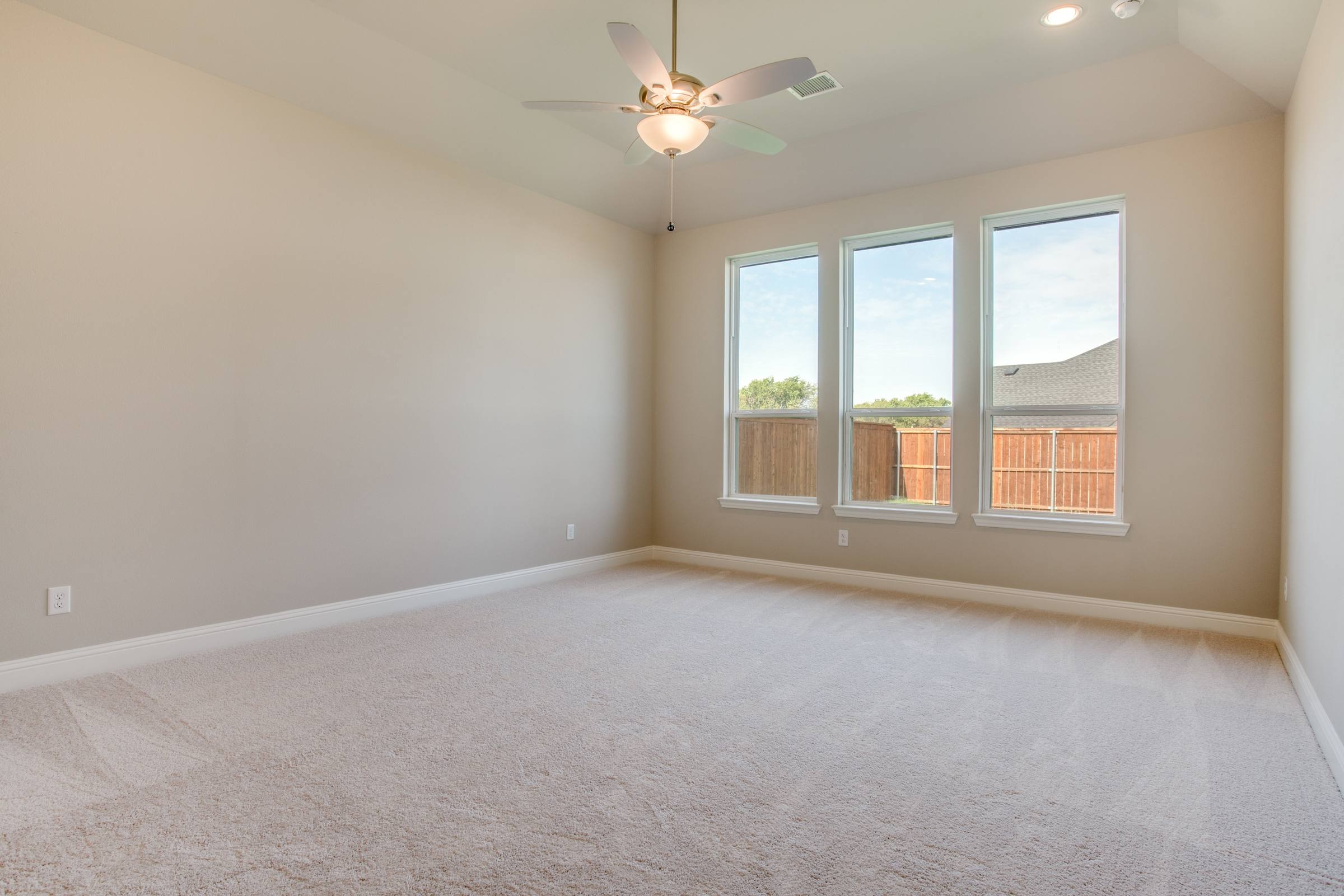 Empty master bedroom with vaulted ceiling and ceiling fan before virtual staging in new construction home in Celina, Texas